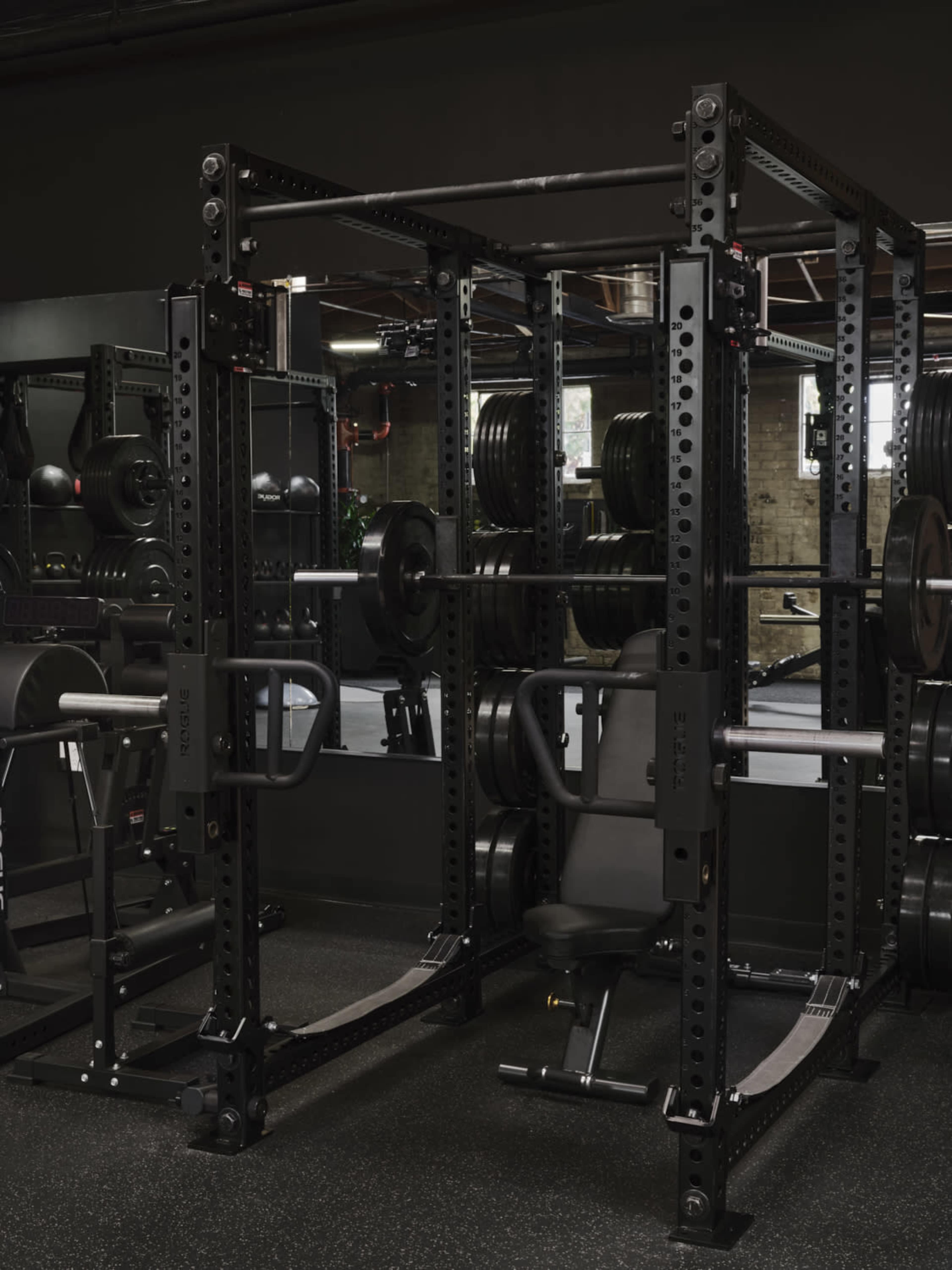 A black weightlifting rack with barbells and a bench in a gym setting.