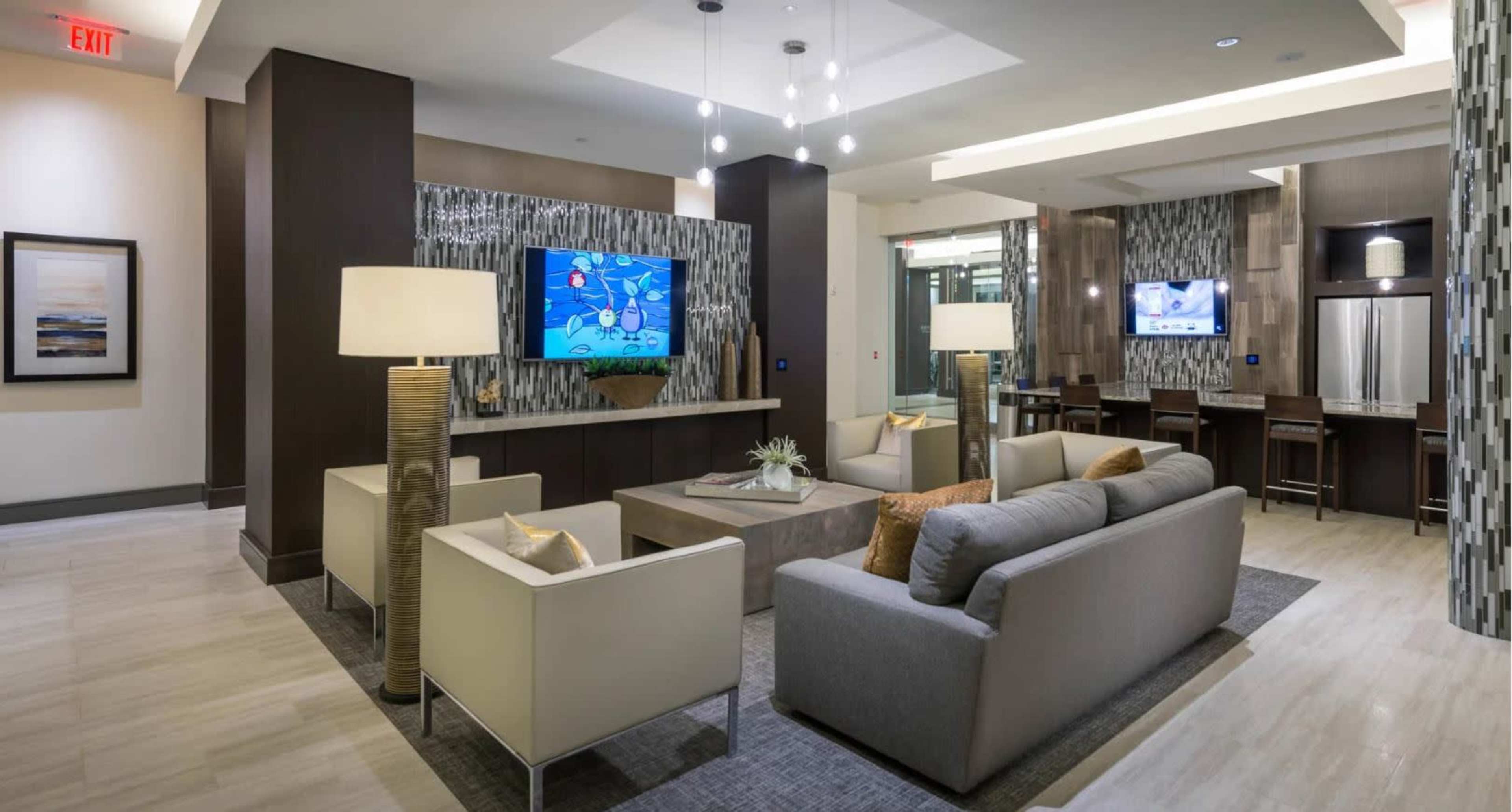 A modern lobby with couches, decorative lighting, and a large television displaying graphics on the wall.