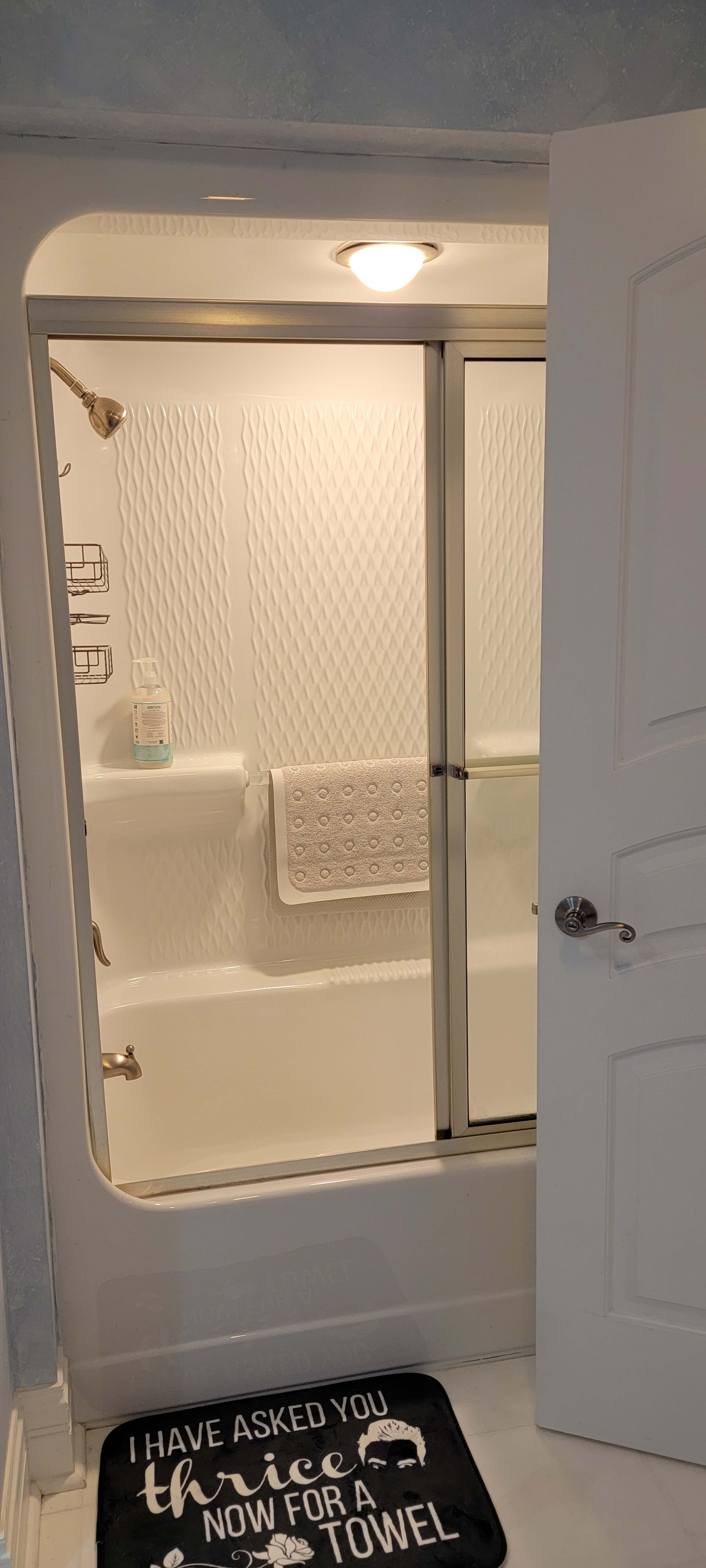 A shower stall with sliding glass doors, a white towel hanging on a rack inside, and a welcome mat placed outside the shower.