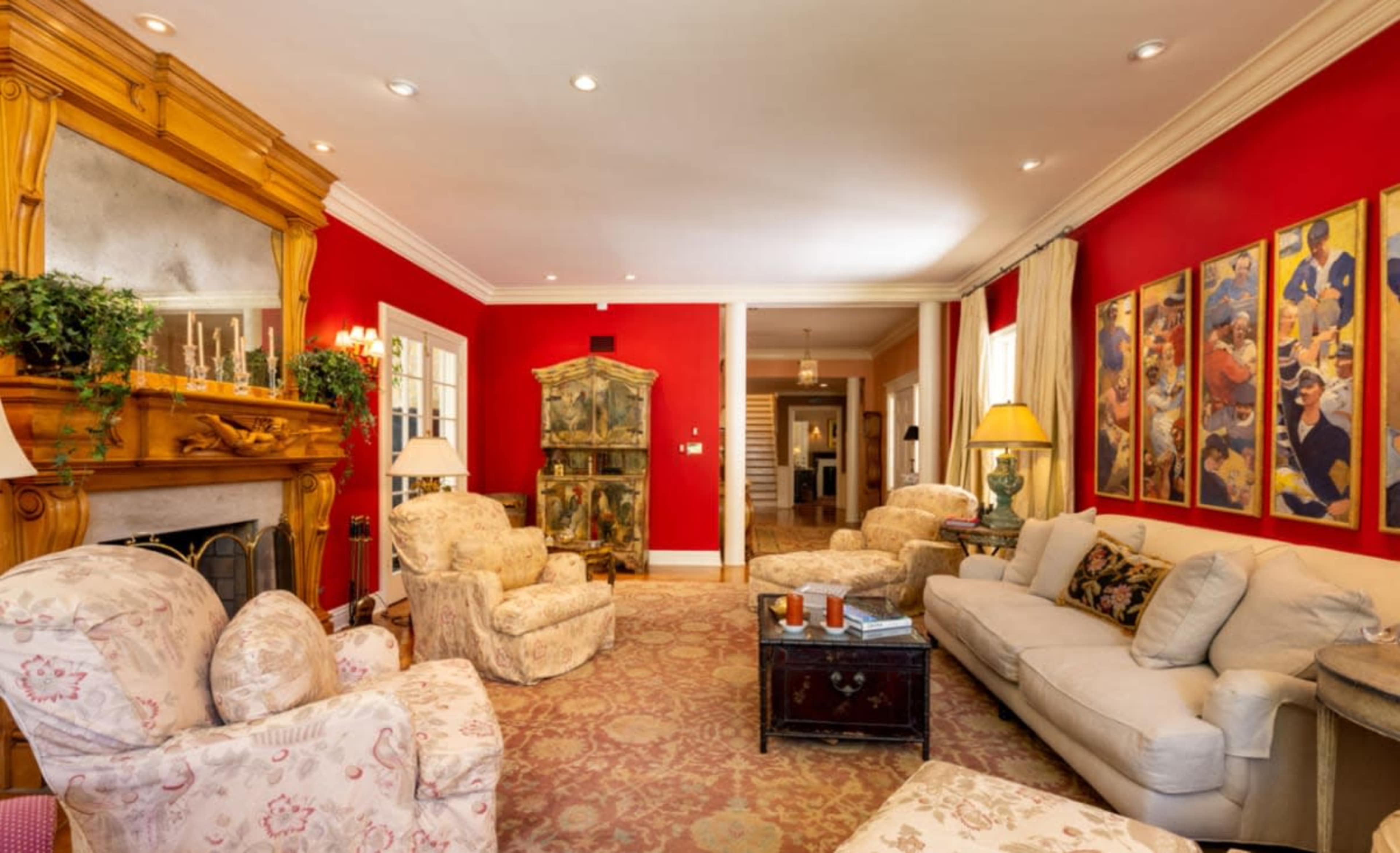 The living room features a red wall, upholstered furniture, a decorative fireplace, and framed artwork.
