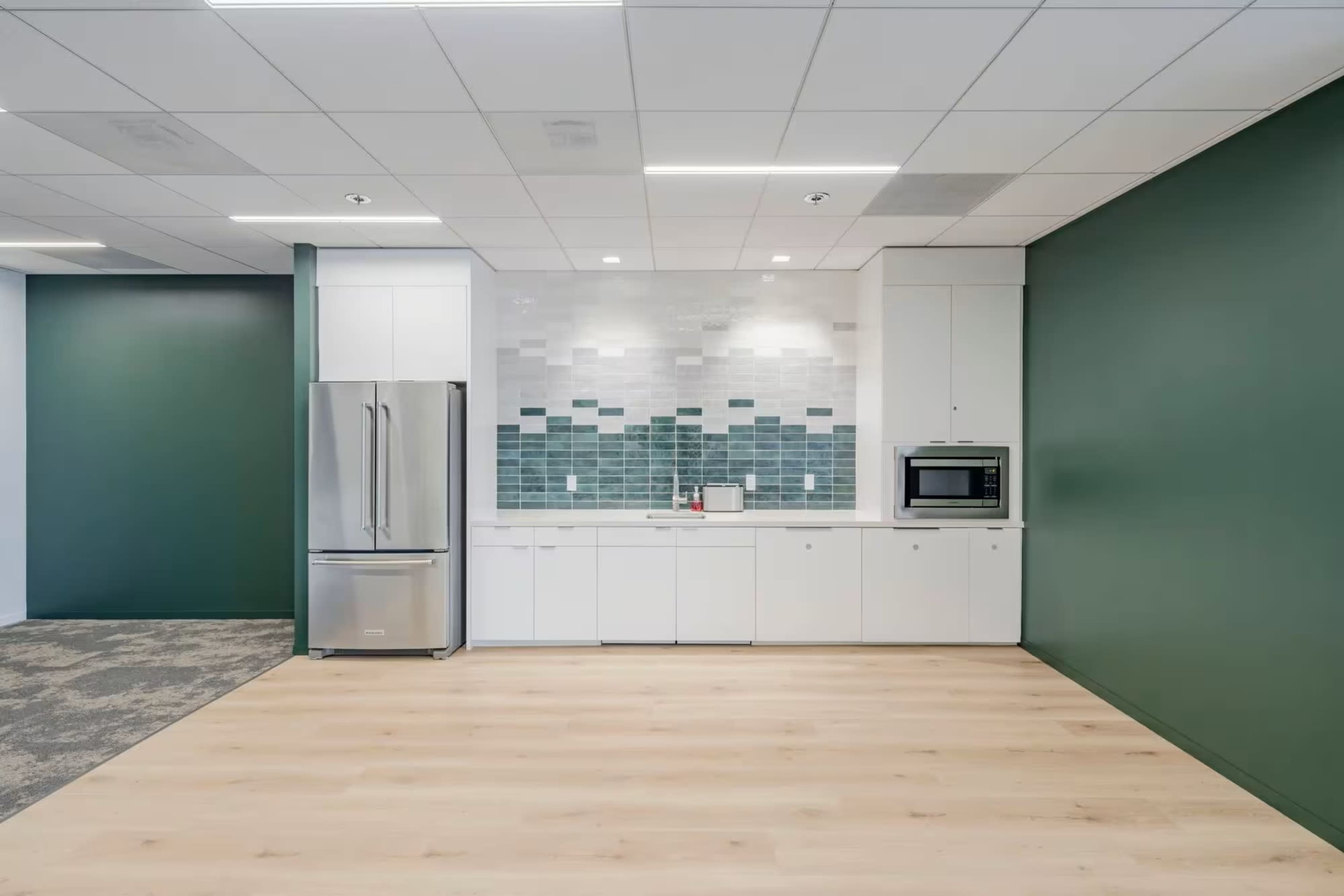 The image shows a modern kitchen space featuring a refrigerator, microwave, and cabinetry with a tiled backsplash.