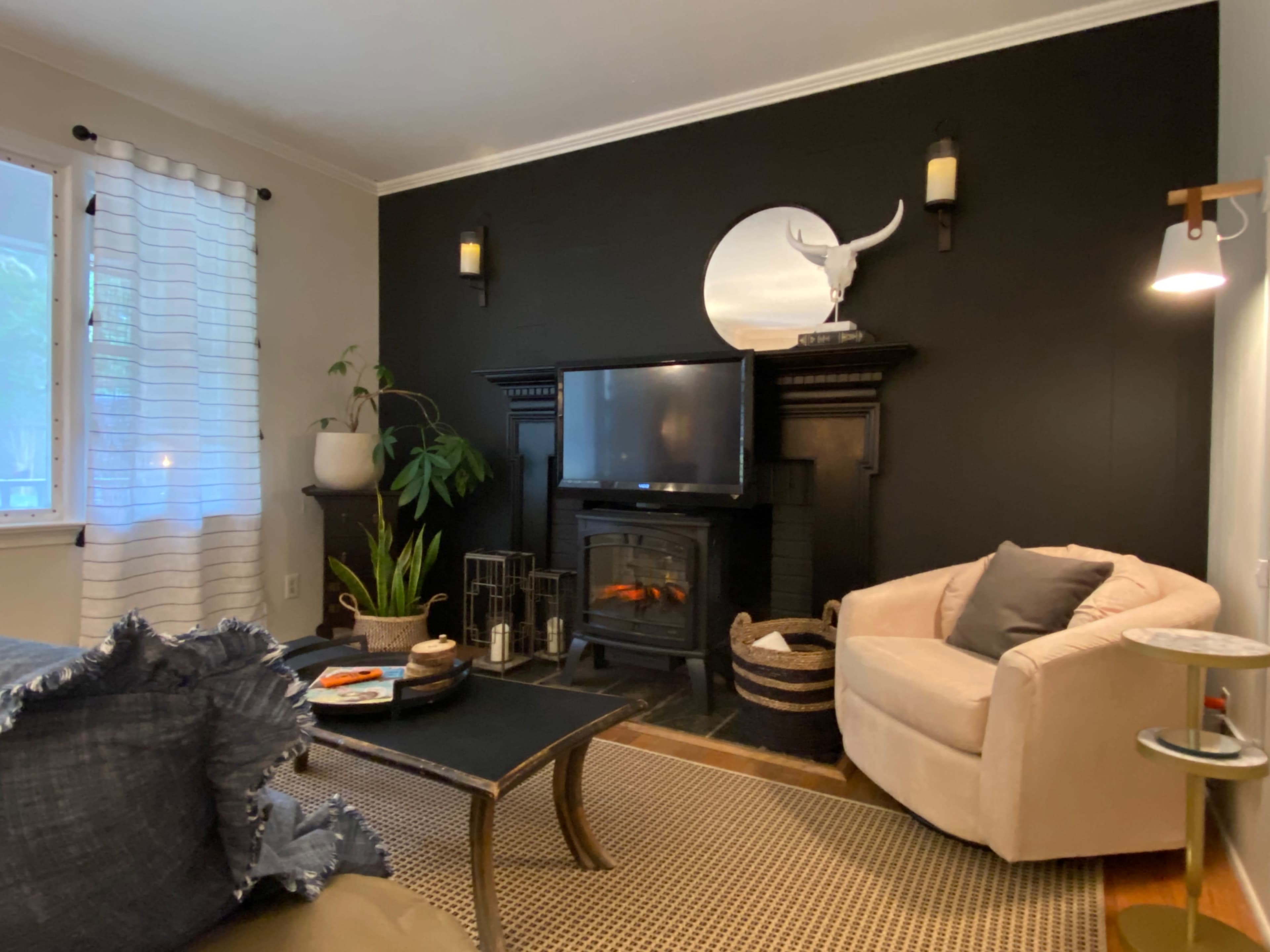 A living room with a black accent wall featuring a fireplace, a television, a beige armchair, and a coffee table with a light-colored rug.