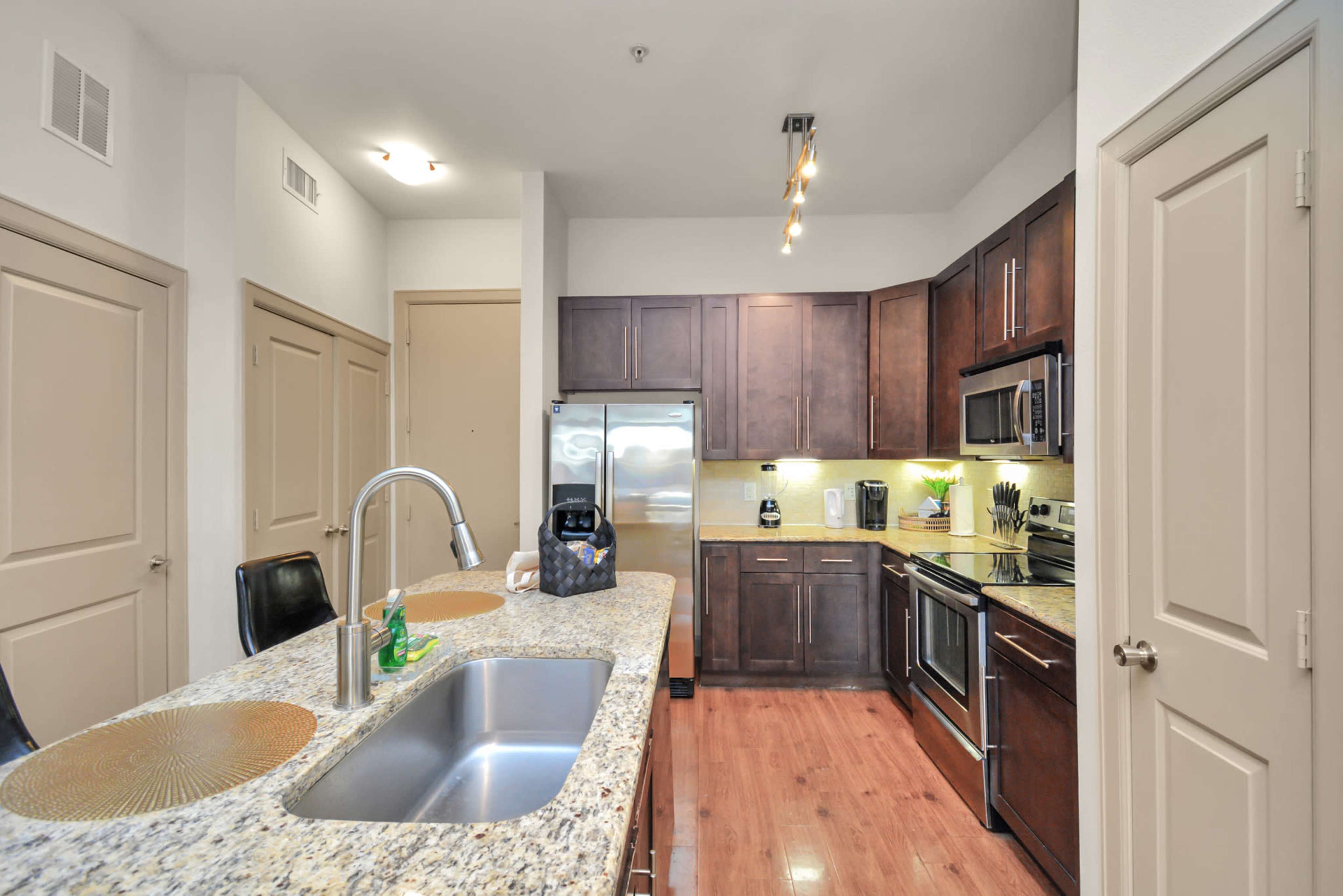A modern kitchen features dark wooden cabinets, stainless steel appliances, and a granite countertop with a double sink.