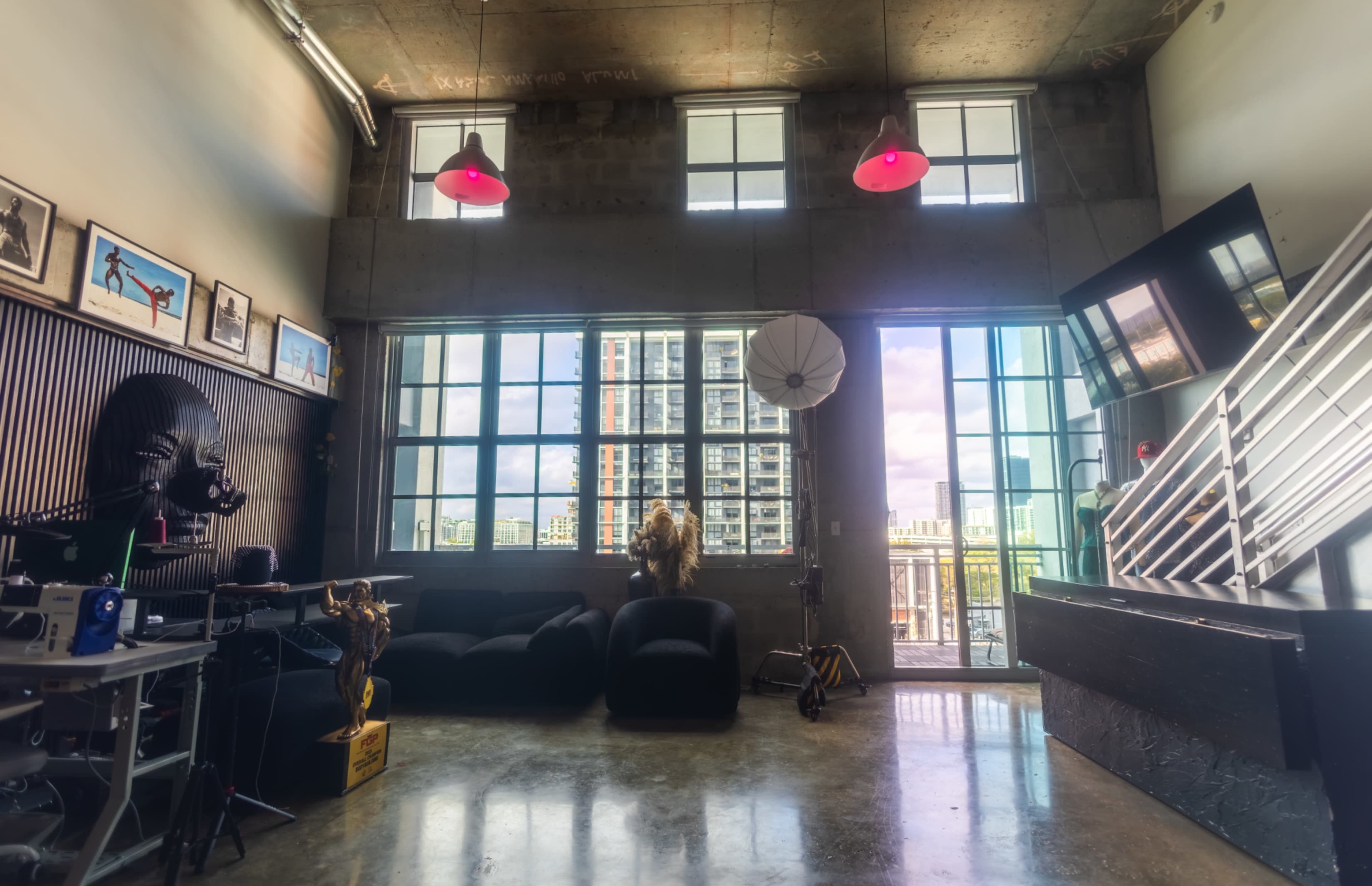 The image shows a modern studio space with large windows, black furniture, a photography backdrop, and artistic decor elements.
