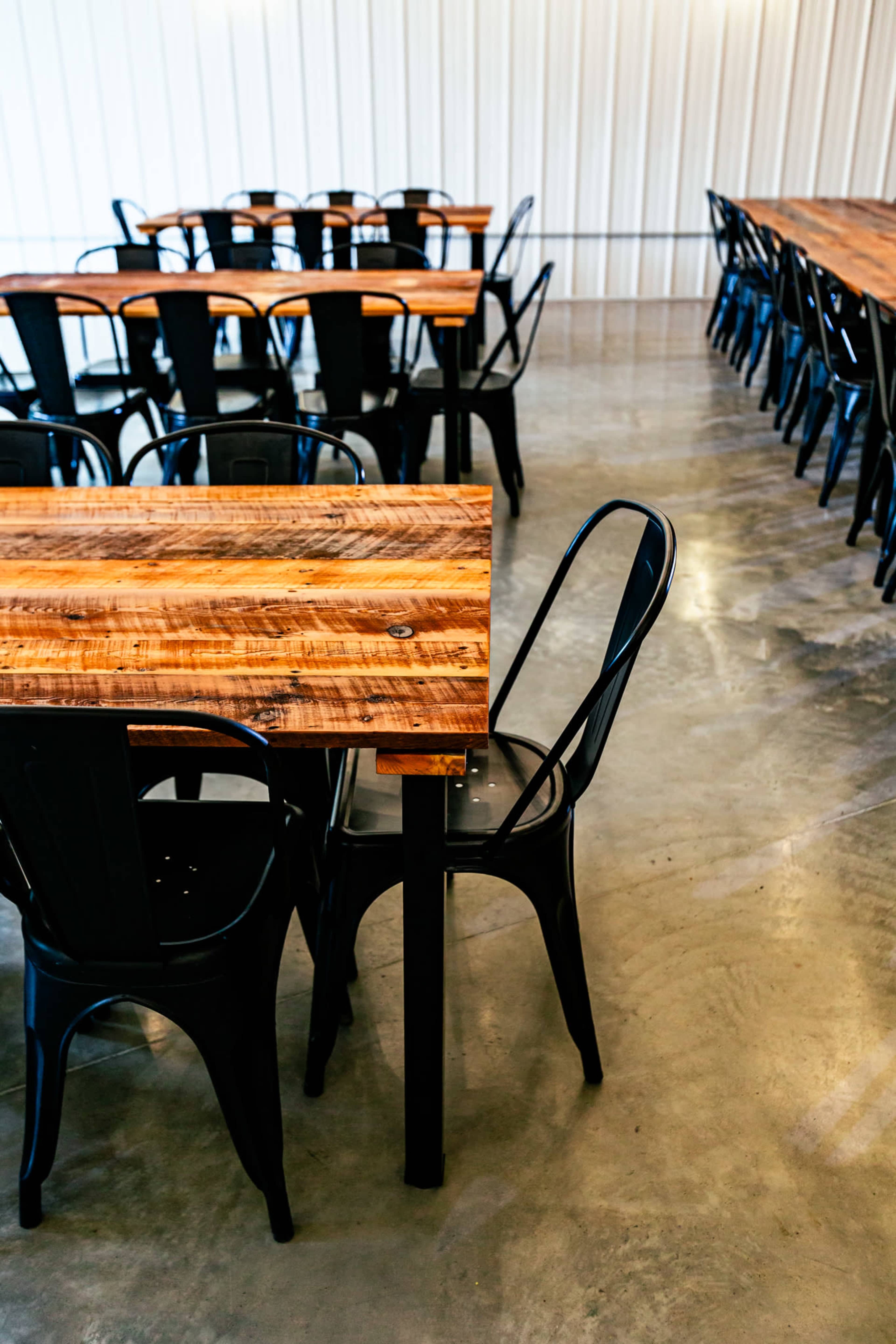 The image shows several wooden tables with black metal chairs arranged in a bright, modern dining space.