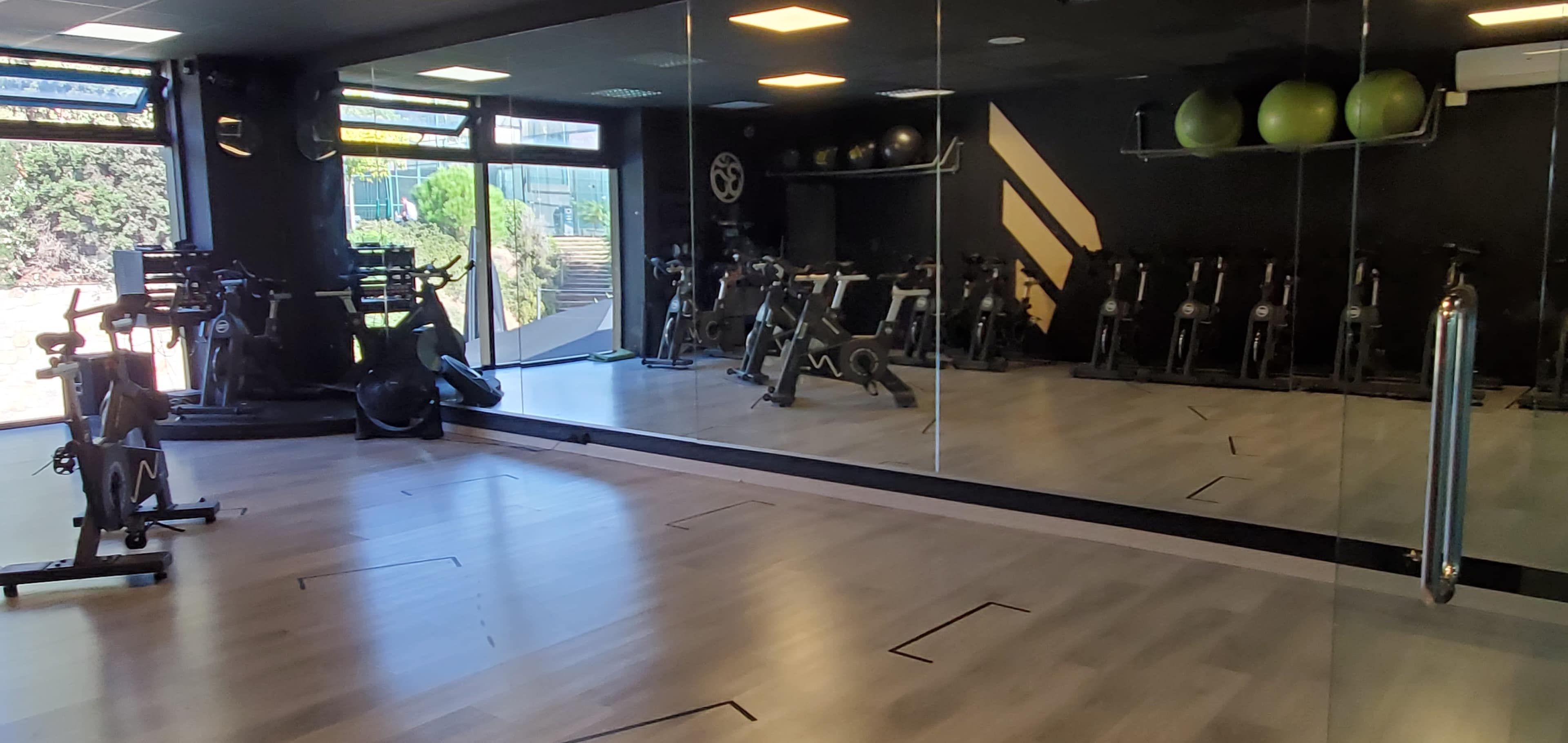 A fitness studio with exercise bikes lined against a wall, large mirrors reflecting the space, and green exercise balls on a shelf.