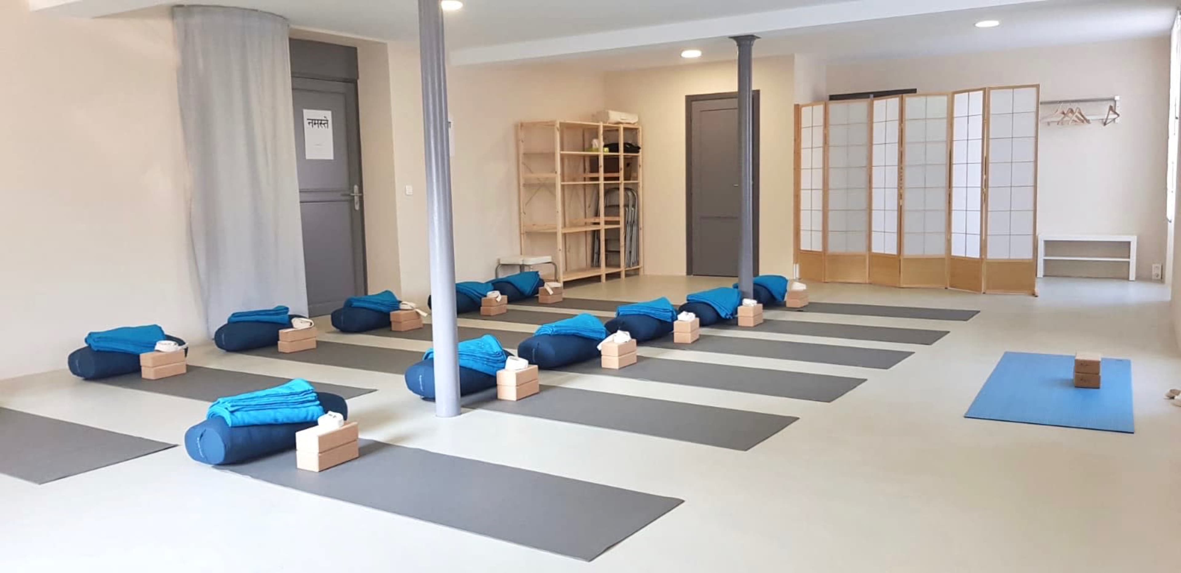 A yoga studio with neatly arranged mats, bolsters, and wooden blocks in a spacious, well-lit room.