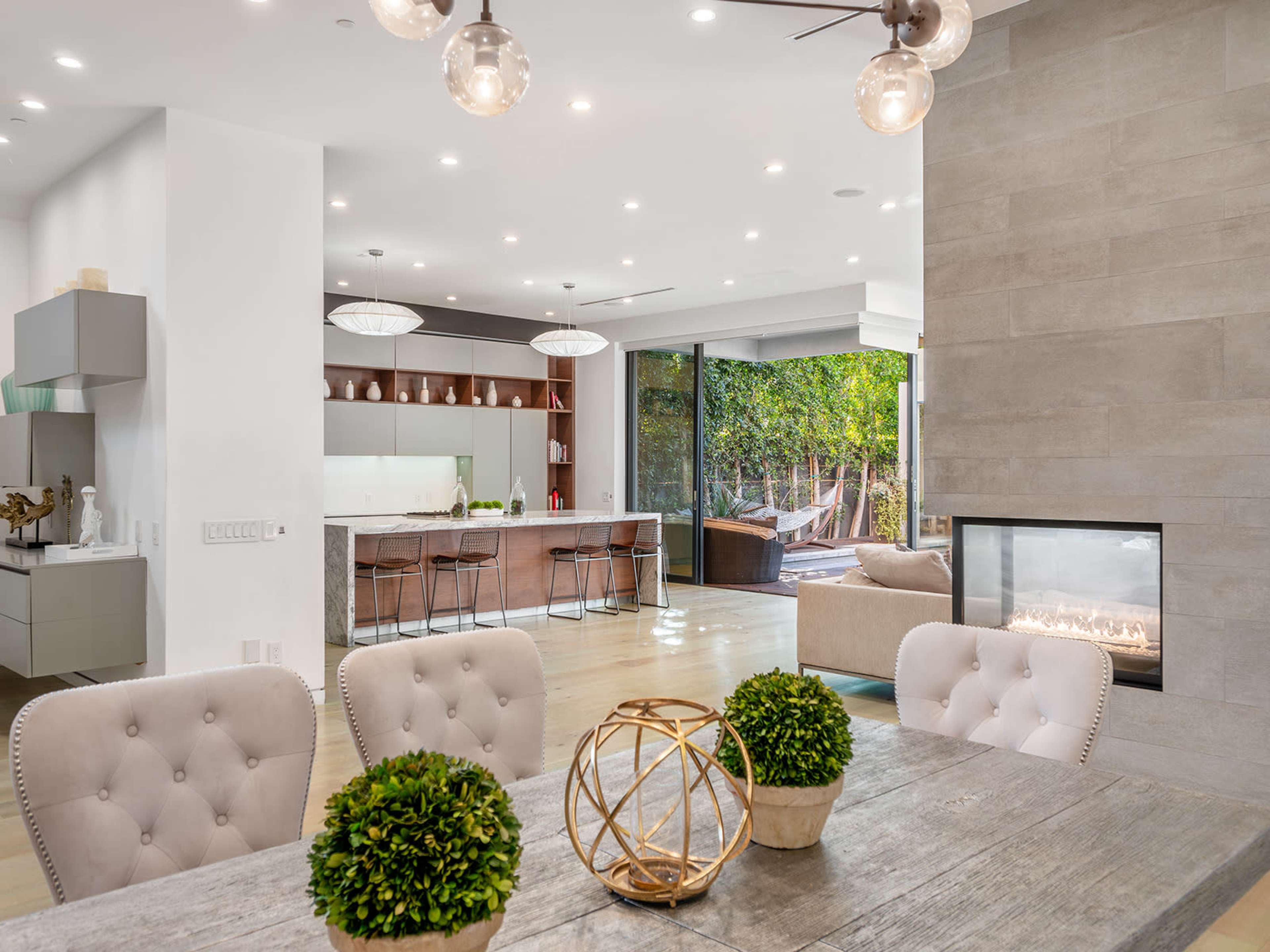 A modern kitchen and dining area with a large sliding glass door that opens to an outdoor space, featuring a fireplace and contemporary furnishings.