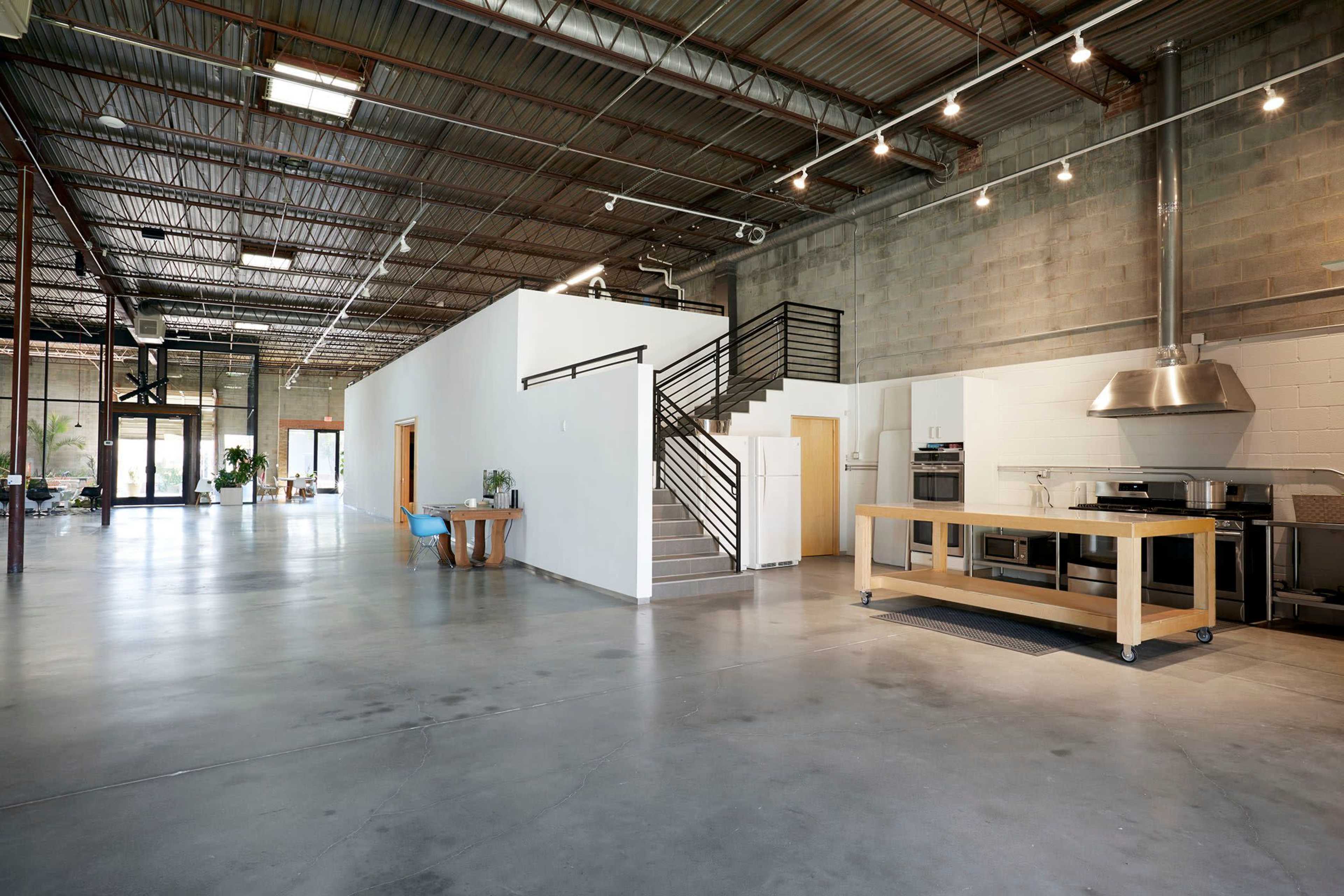 A spacious industrial-style interior with polished concrete floors, a modern kitchen area, and stair access to a second level.