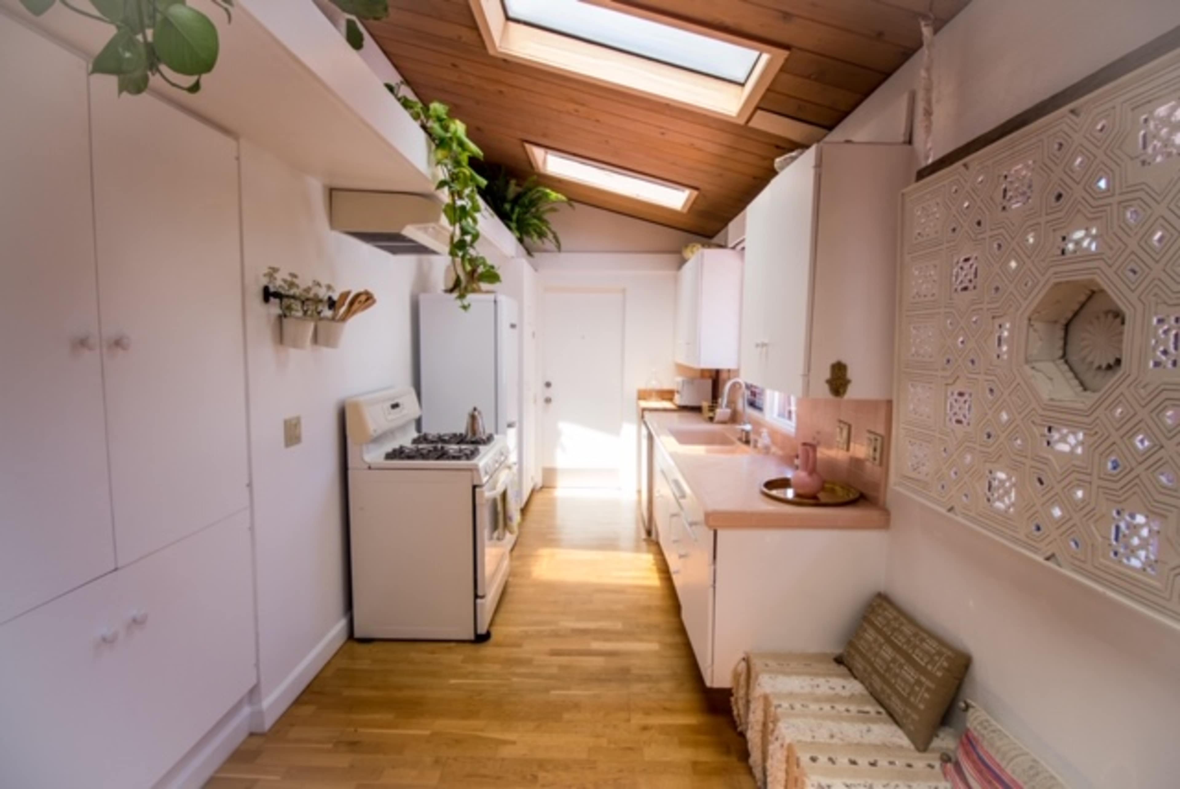 The image shows a narrow kitchen with skylights, white cabinets, a gas stove, and wooden flooring.