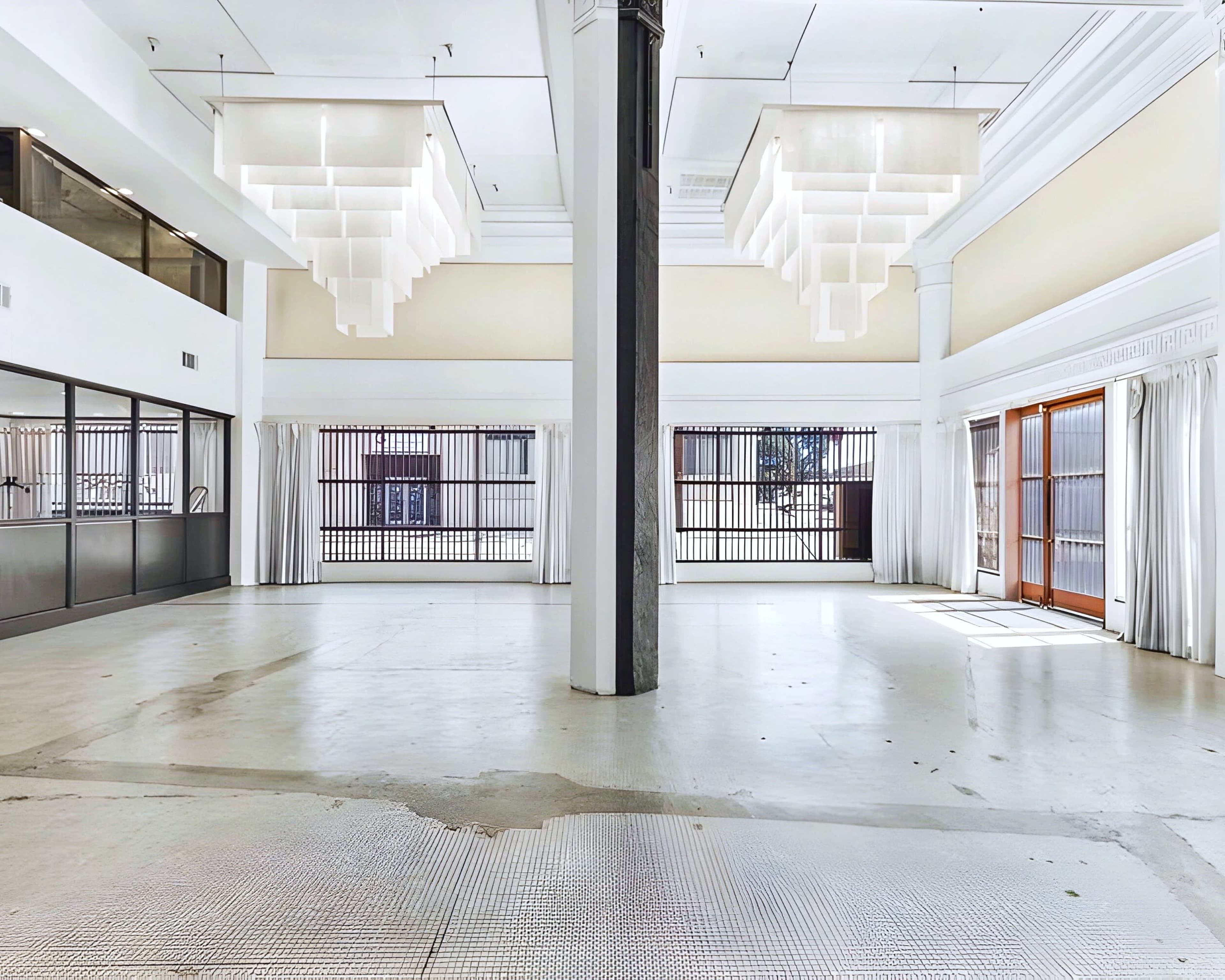 The image shows an empty, spacious interior with large windows, tall ceilings, and modern light fixtures.