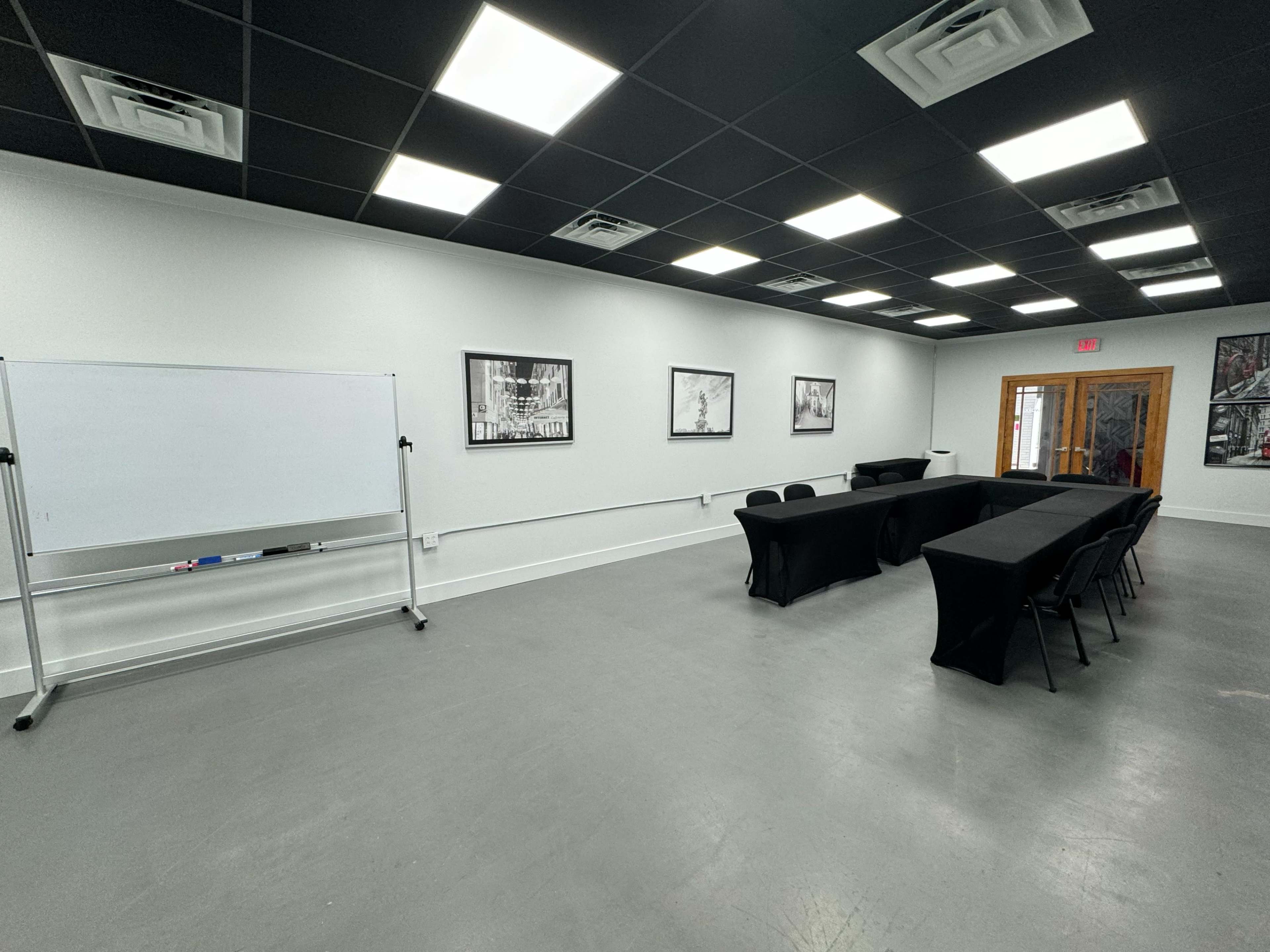 The image shows a conference room with a whiteboard, several black tables arranged in a U-shape, and framed black-and-white photographs on the walls.