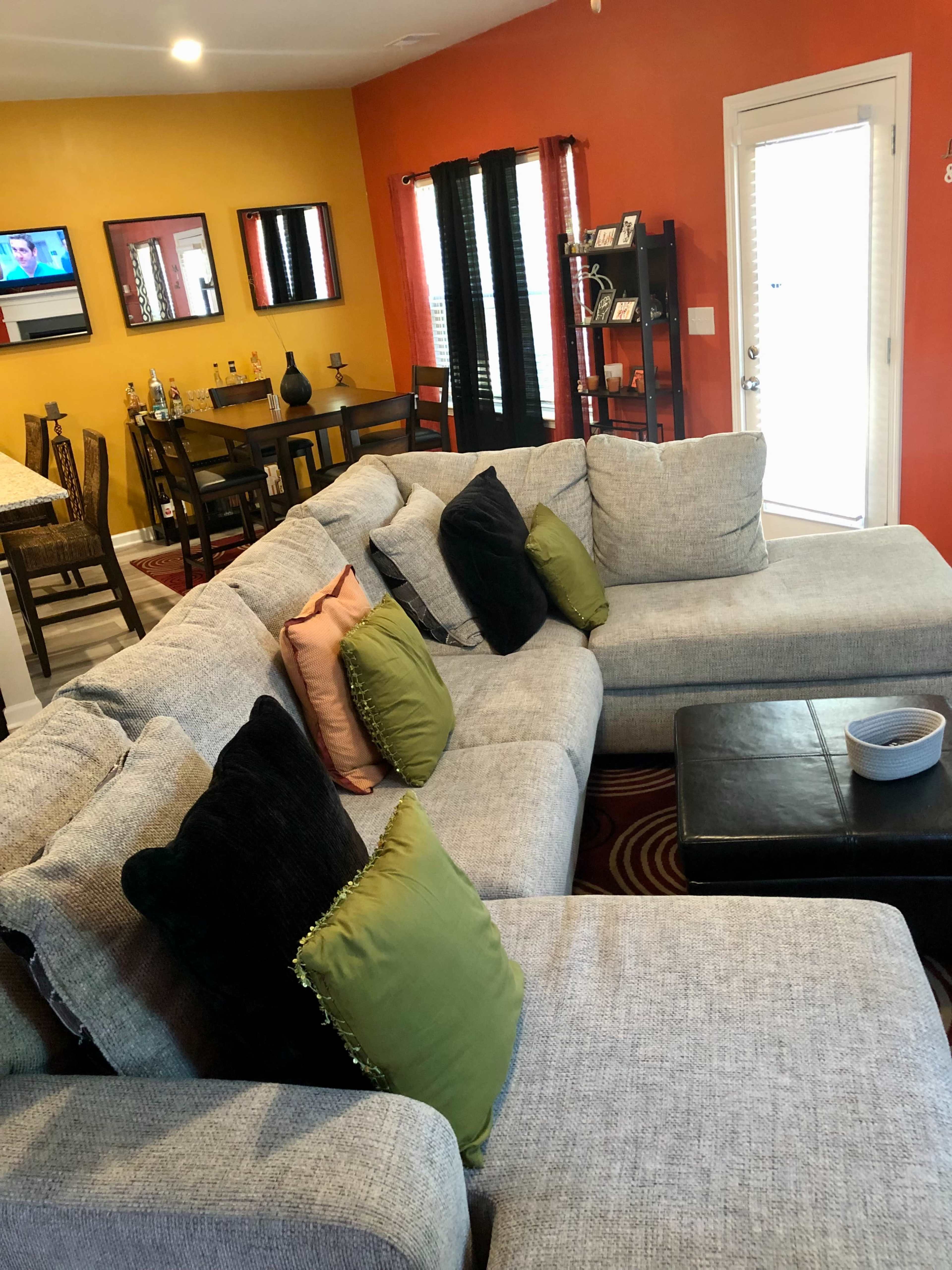 A cozy living room area with a large gray sectional sofa adorned with several colorful pillows, a coffee table, and a door leading outside.