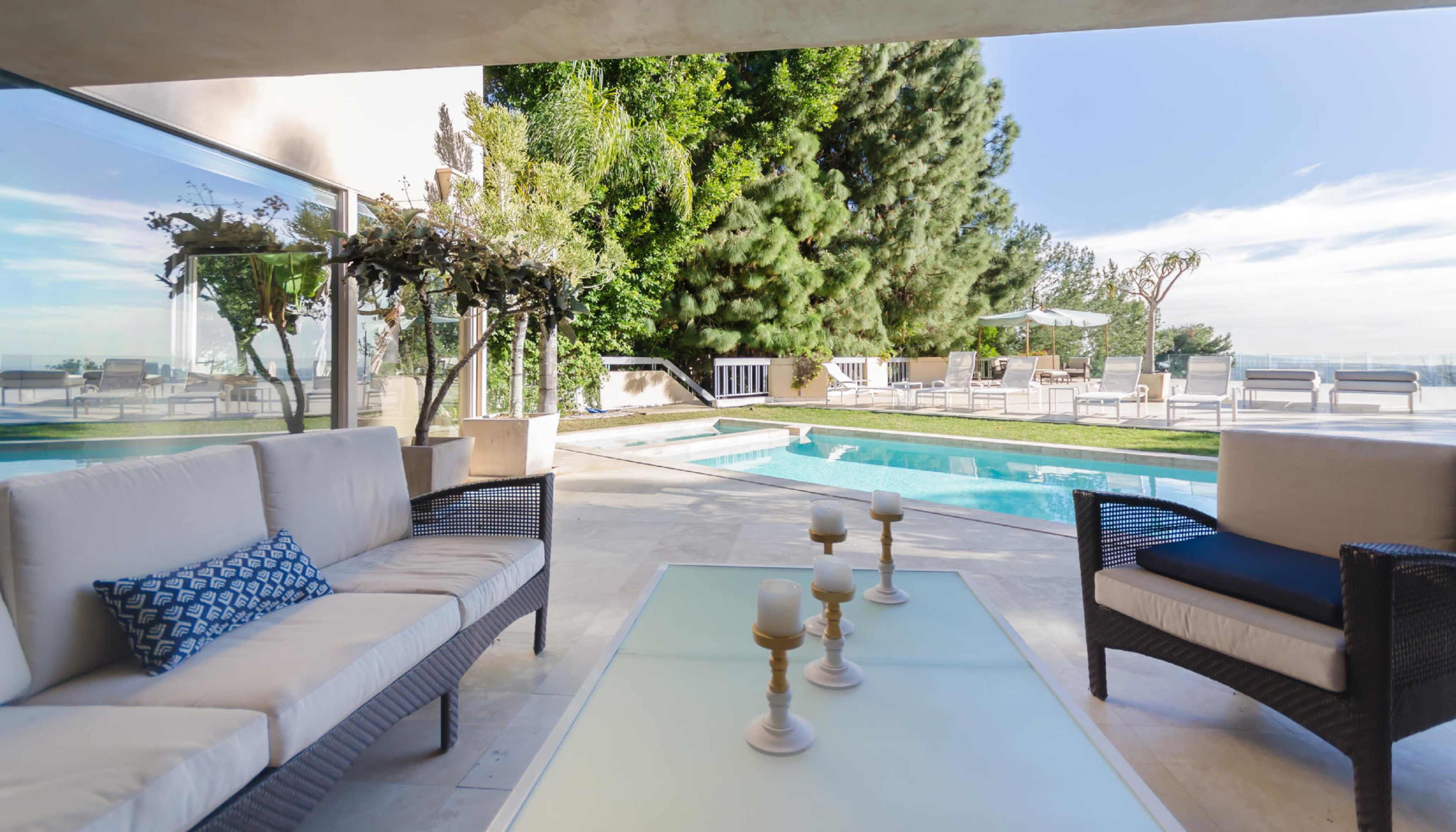 A patio with two seating areas overlooking a swimming pool surrounded by greenery.