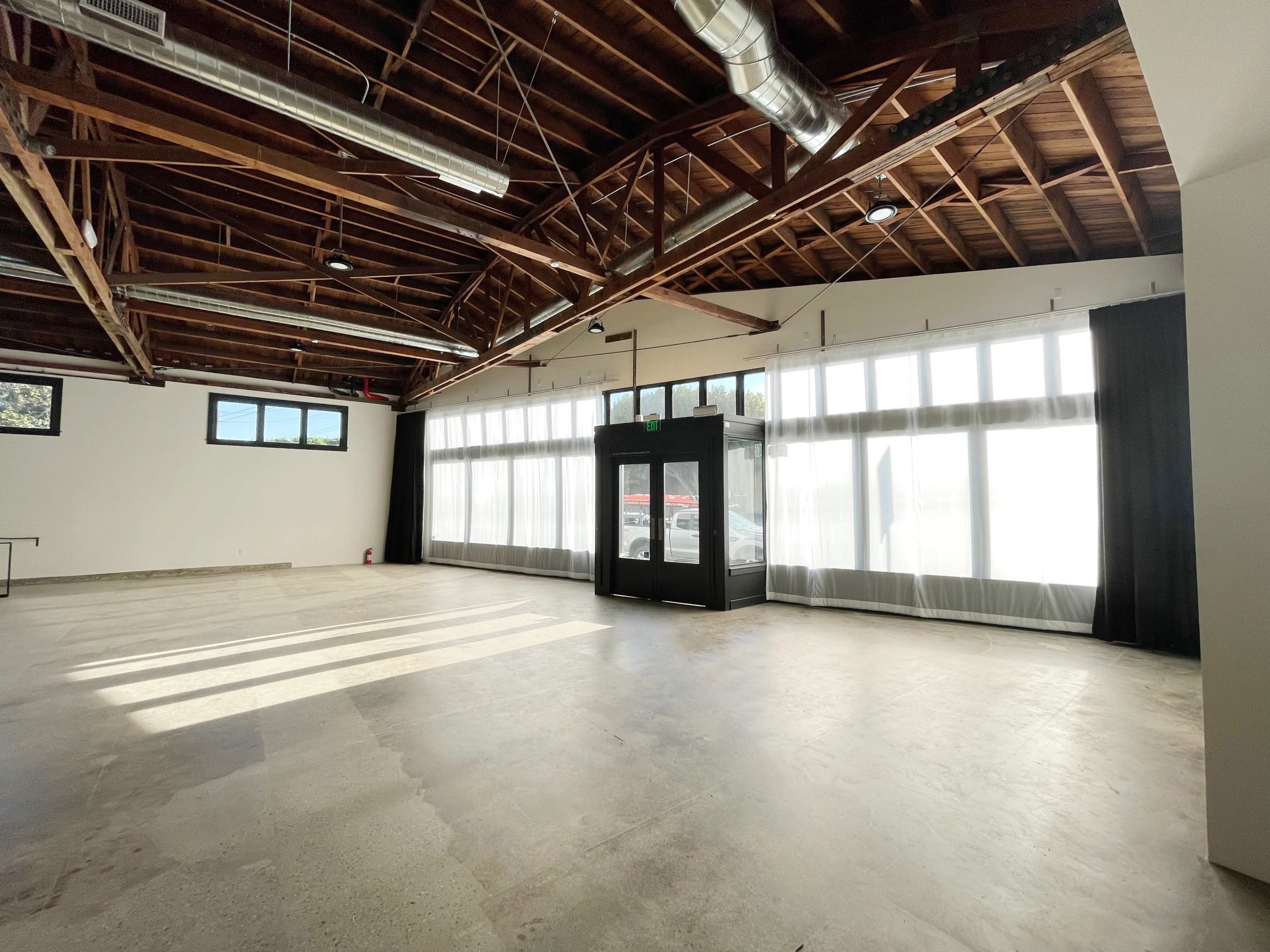 An empty, spacious interior with high wooden beams and large windows allowing natural light to fill the room.