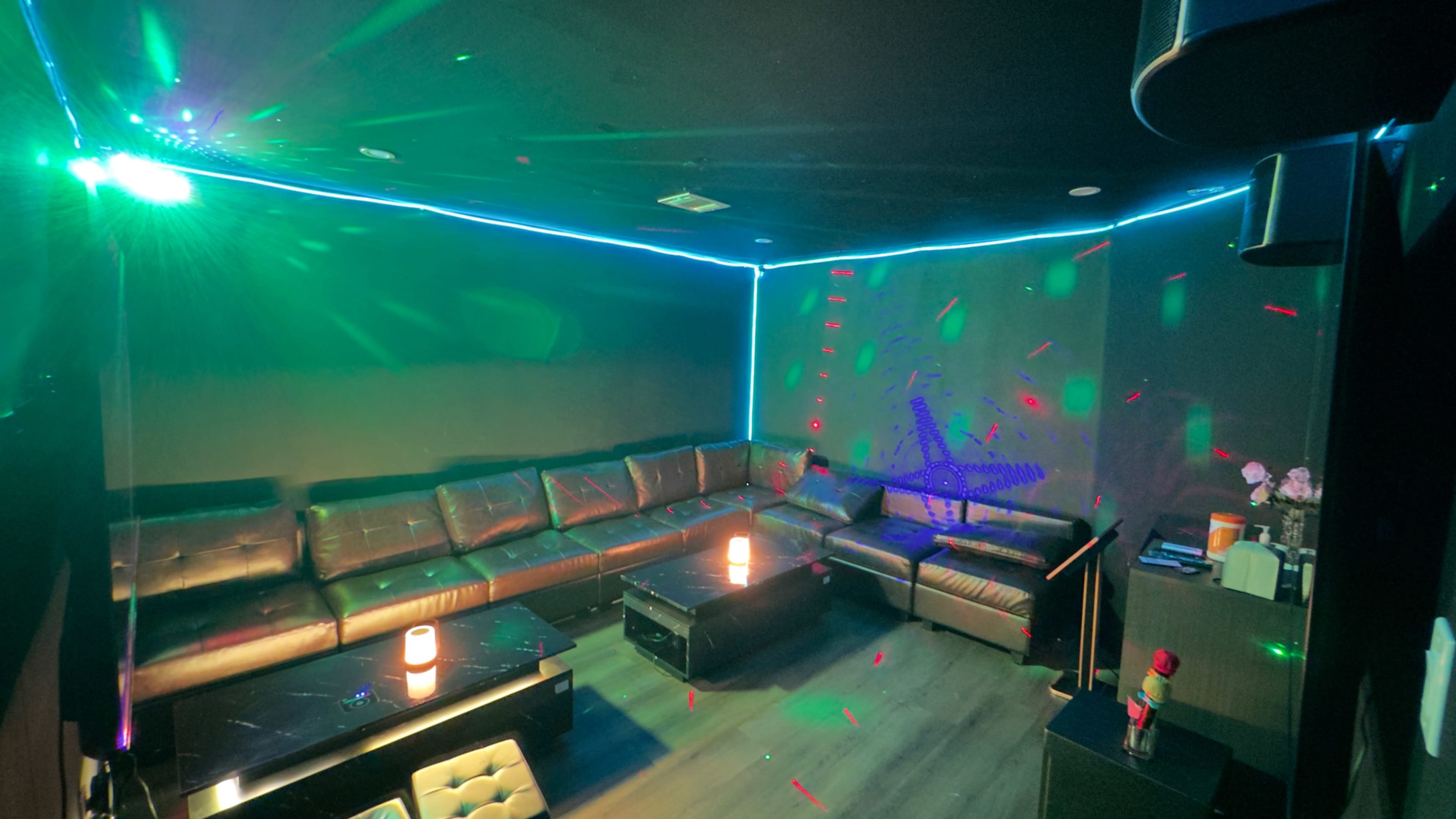 The image shows a dimly lit lounge area with leather couches and colorful light projections on the walls.