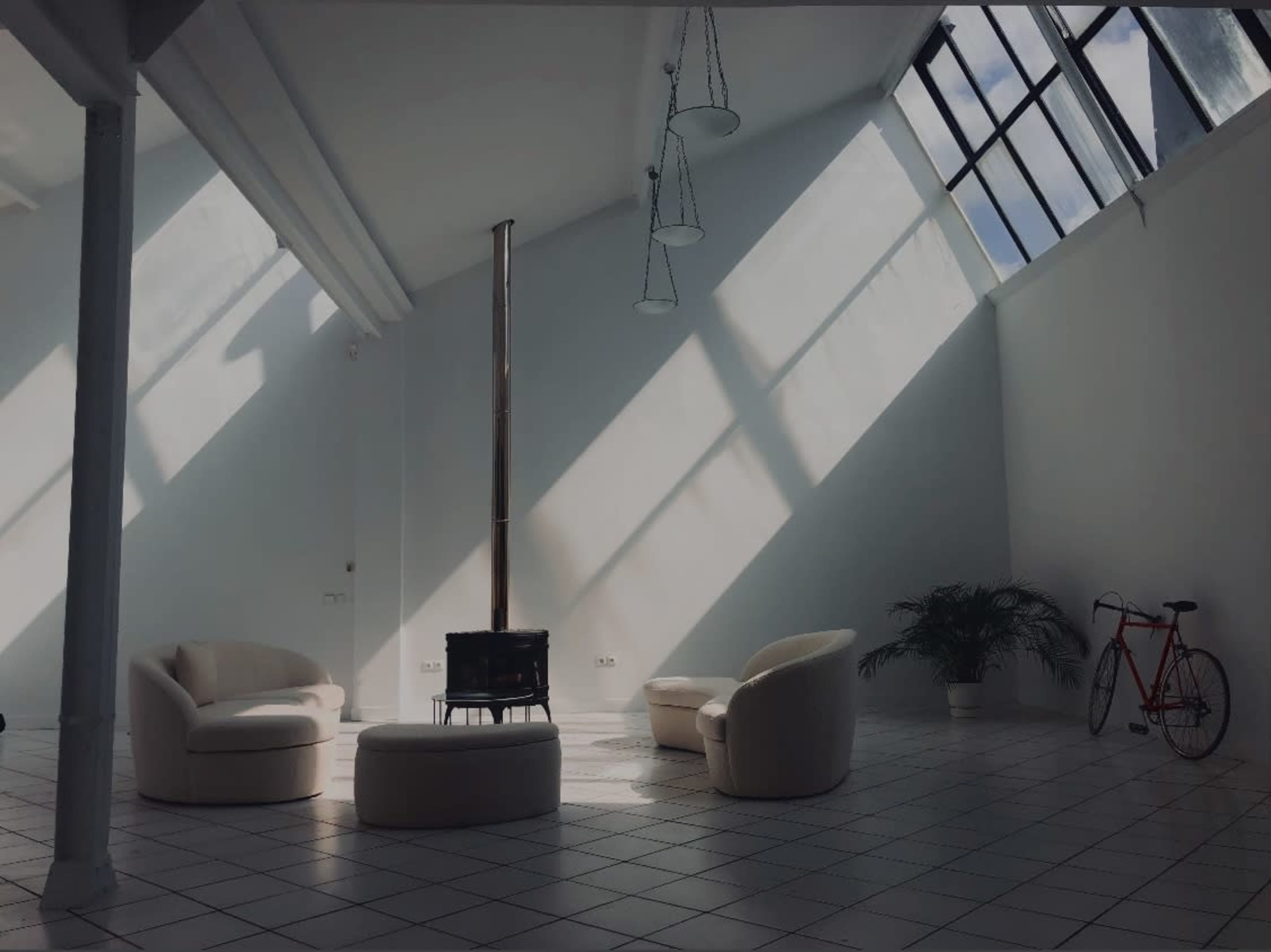 A bright, modern room with two circular chairs, a round table, a wood-burning stove, a potted plant, and a bicycle against a white wall.