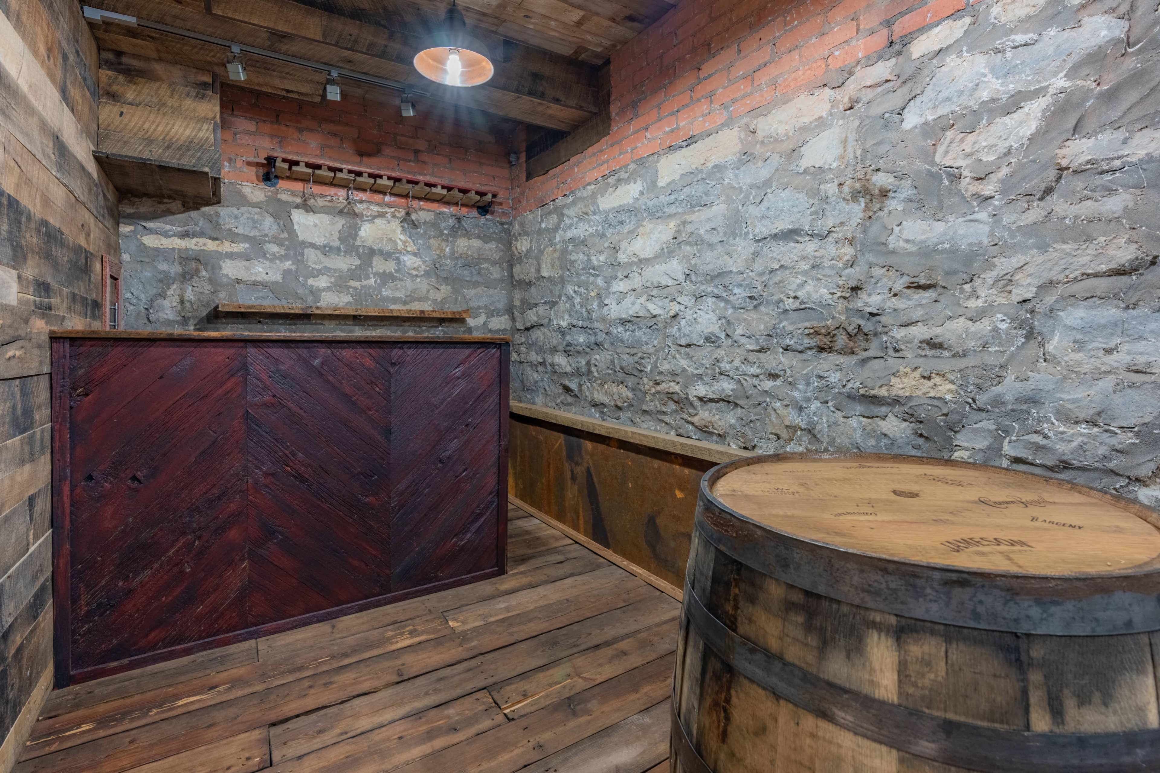 An interior space with rustic wooden walls, a dark wooden bar, and a barrel, set against a backdrop of exposed stone.