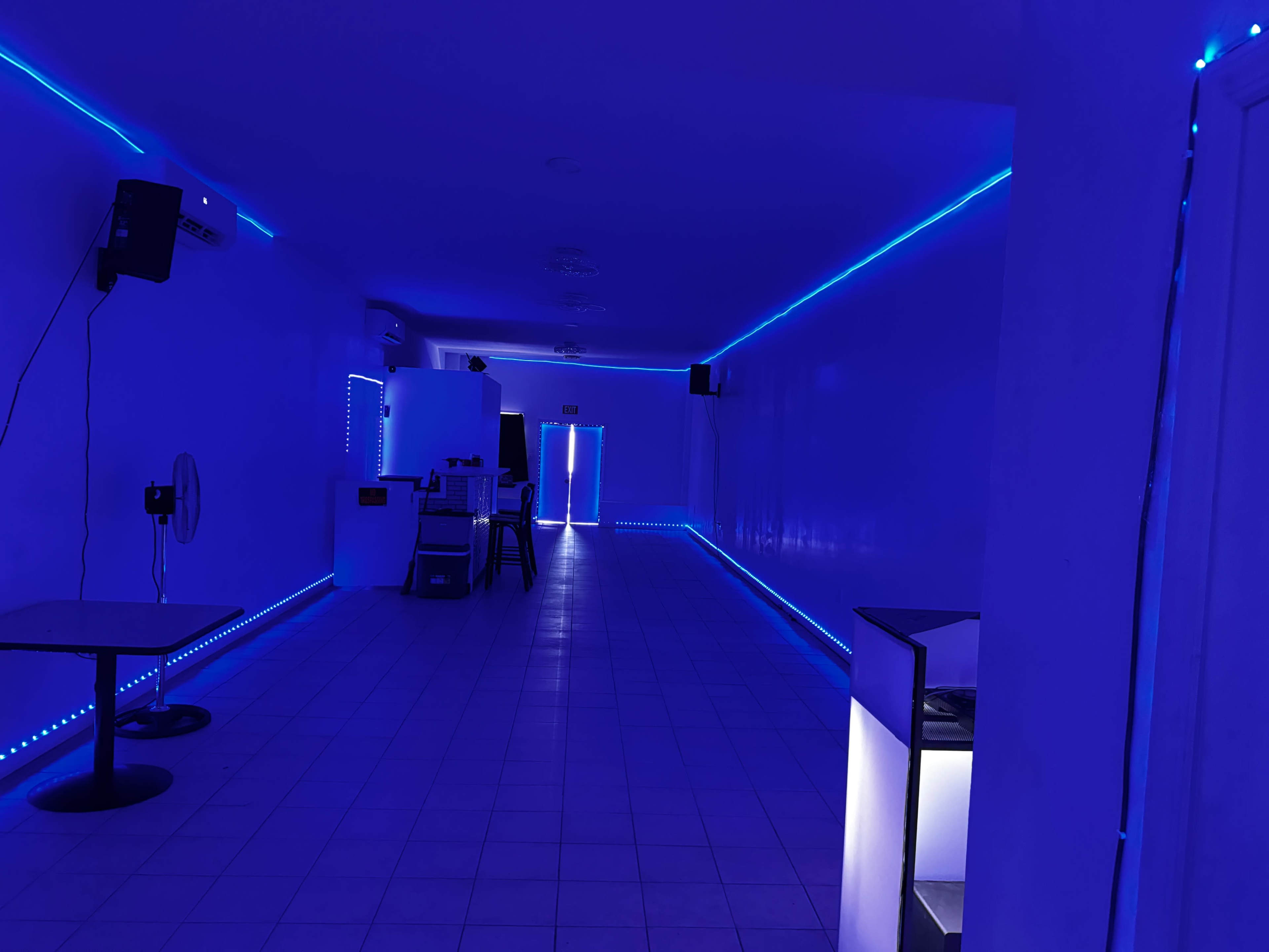 The image shows a dimly lit room with blue LED strip lighting along the walls, featuring a fan and a table on the left side.