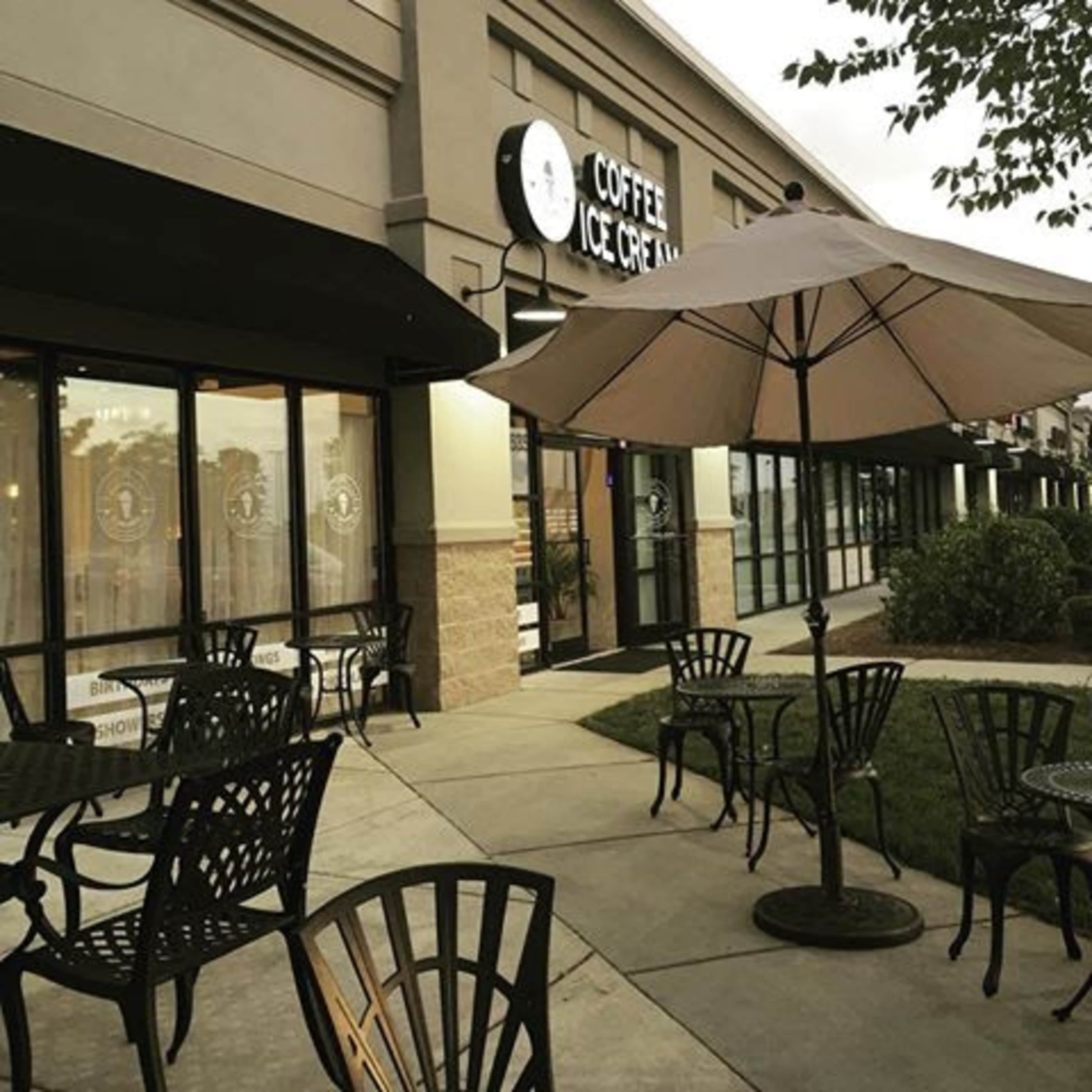 A coffee and ice cream shop features outdoor seating under an umbrella alongside a walkway.