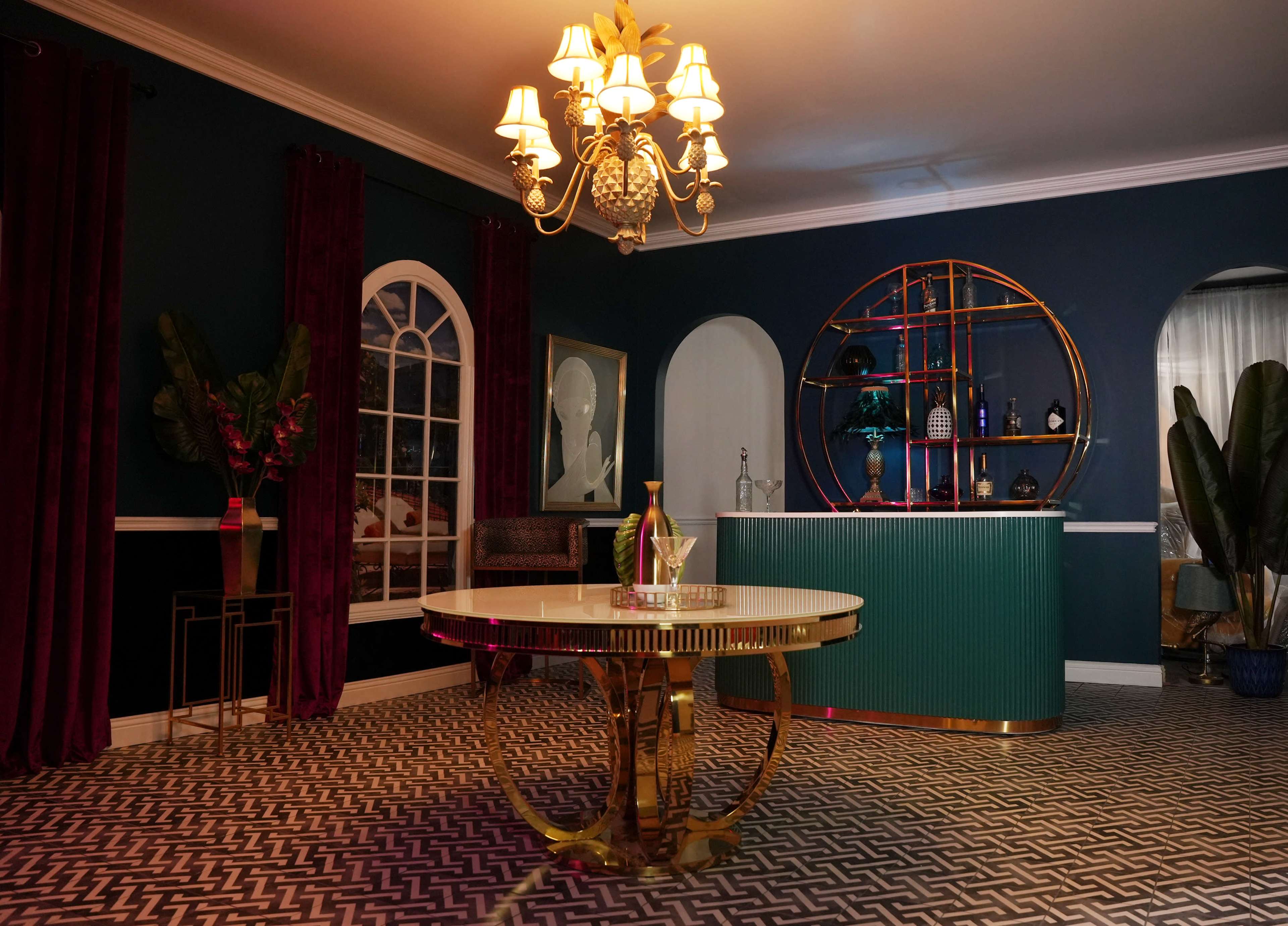 The image depicts an elegantly styled interior featuring a green bar against a blue wall, a round dining table, and decorative lighting.