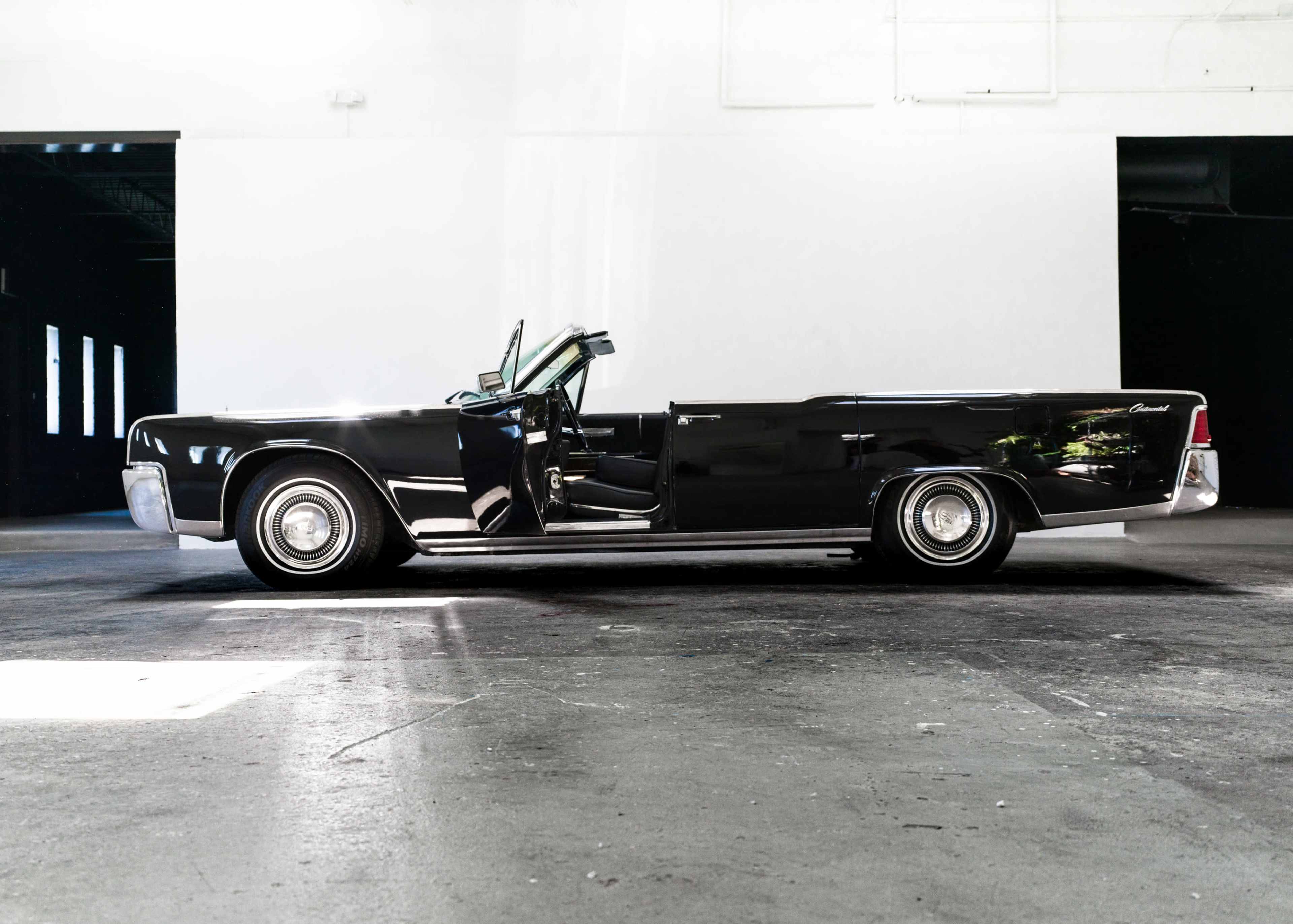 The image shows a classic black convertible car parked in an empty industrial space.