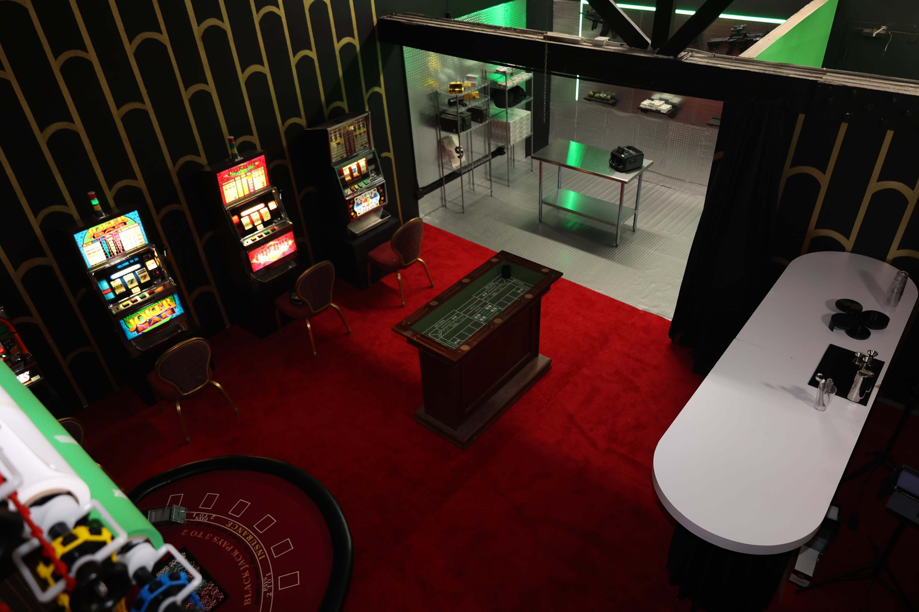 A gaming room featuring slot machines, a roulette table, and a bar area with a white counter.