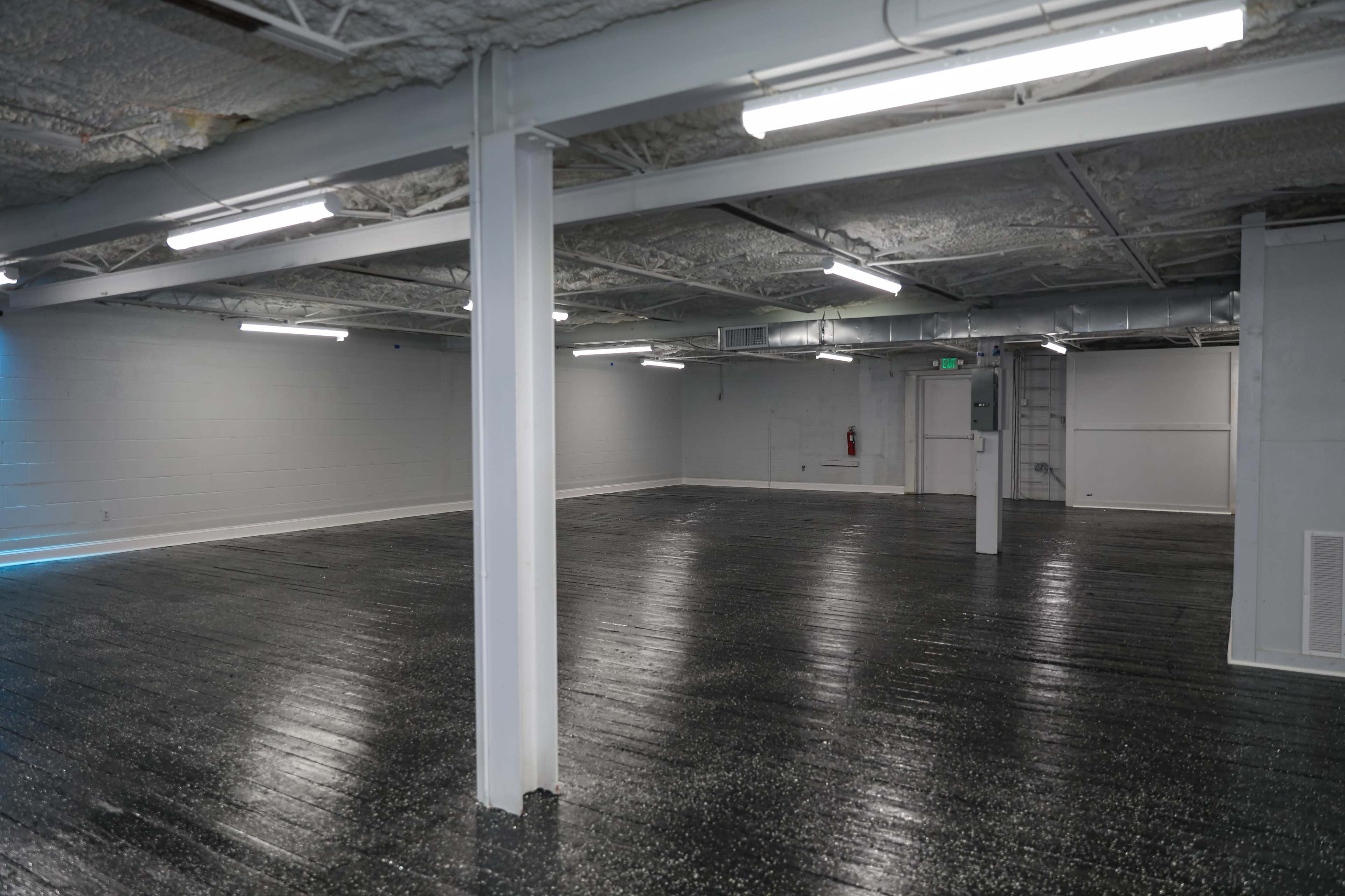 The image shows an empty, industrial-style interior space with exposed beams and polished black flooring.