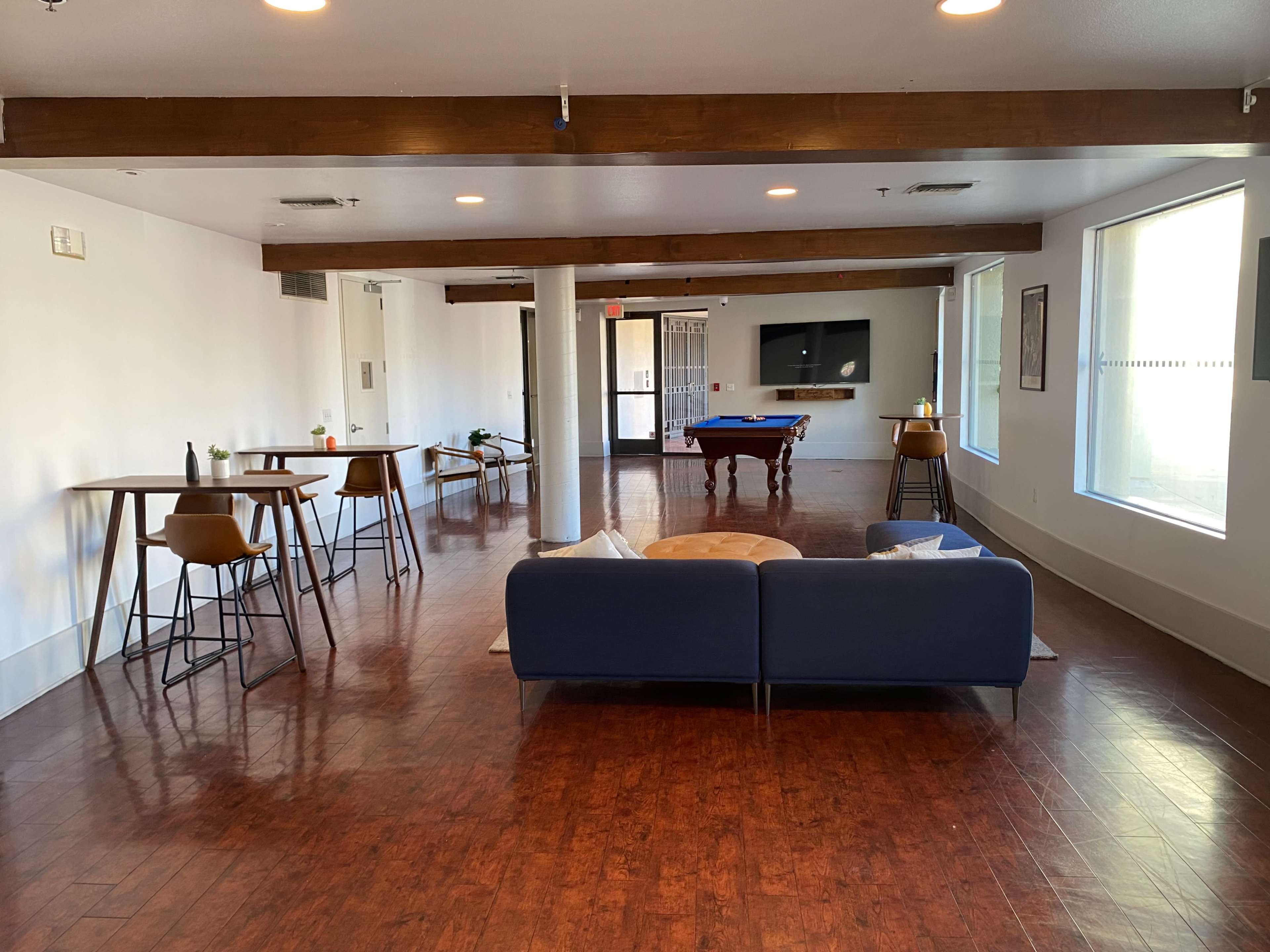 The image shows a spacious indoor lounge area with a pool table, seating arrangements, and large windows illuminating the space.