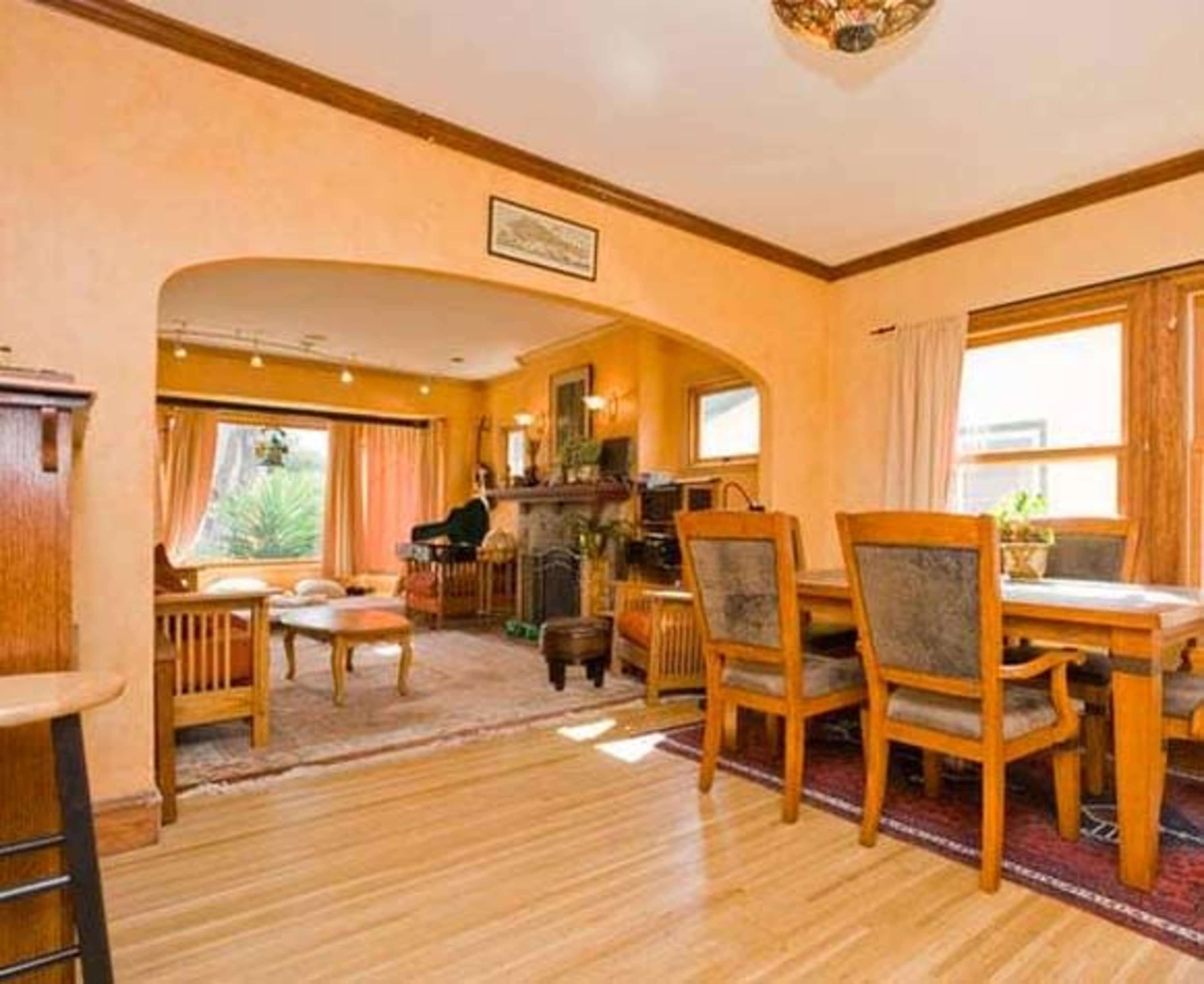 A well-lit dining area with wooden furniture, an arched entryway, and a view of a living room featuring a fireplace and large windows.