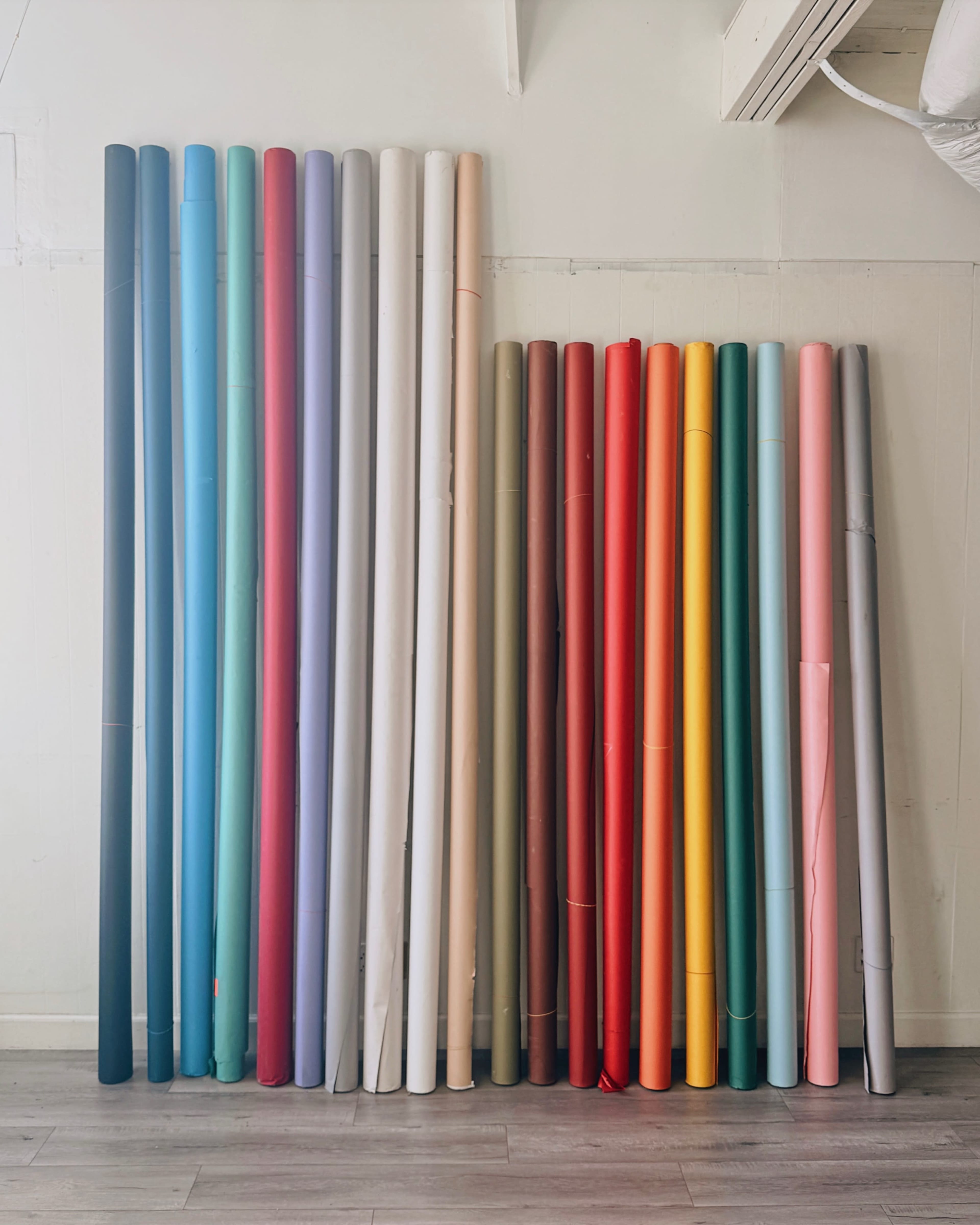A collection of rolled paper or vinyl in various colors stands upright against a wall.