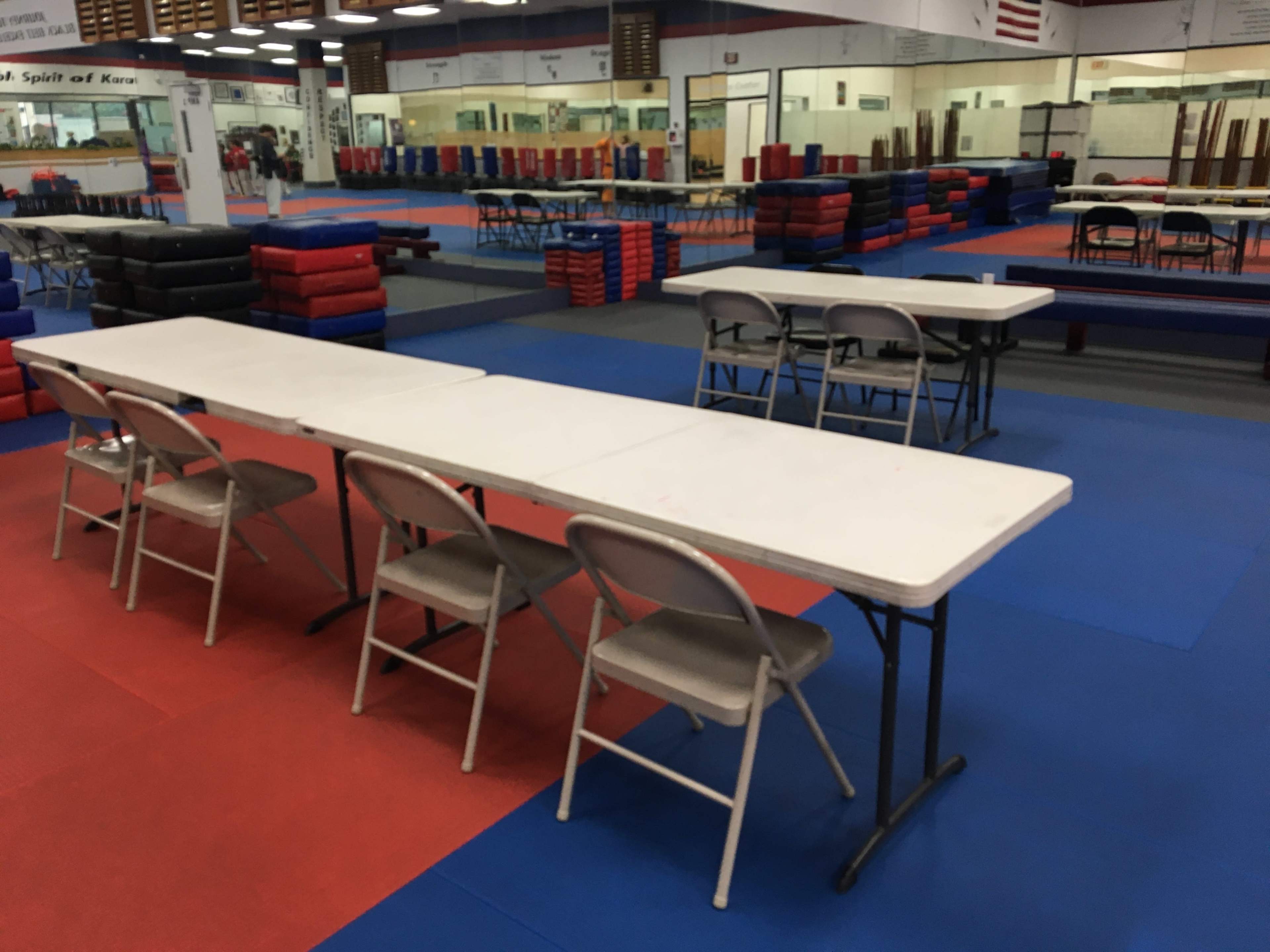 A gymnasium with multiple folding tables and chairs arranged on a colorful matting.