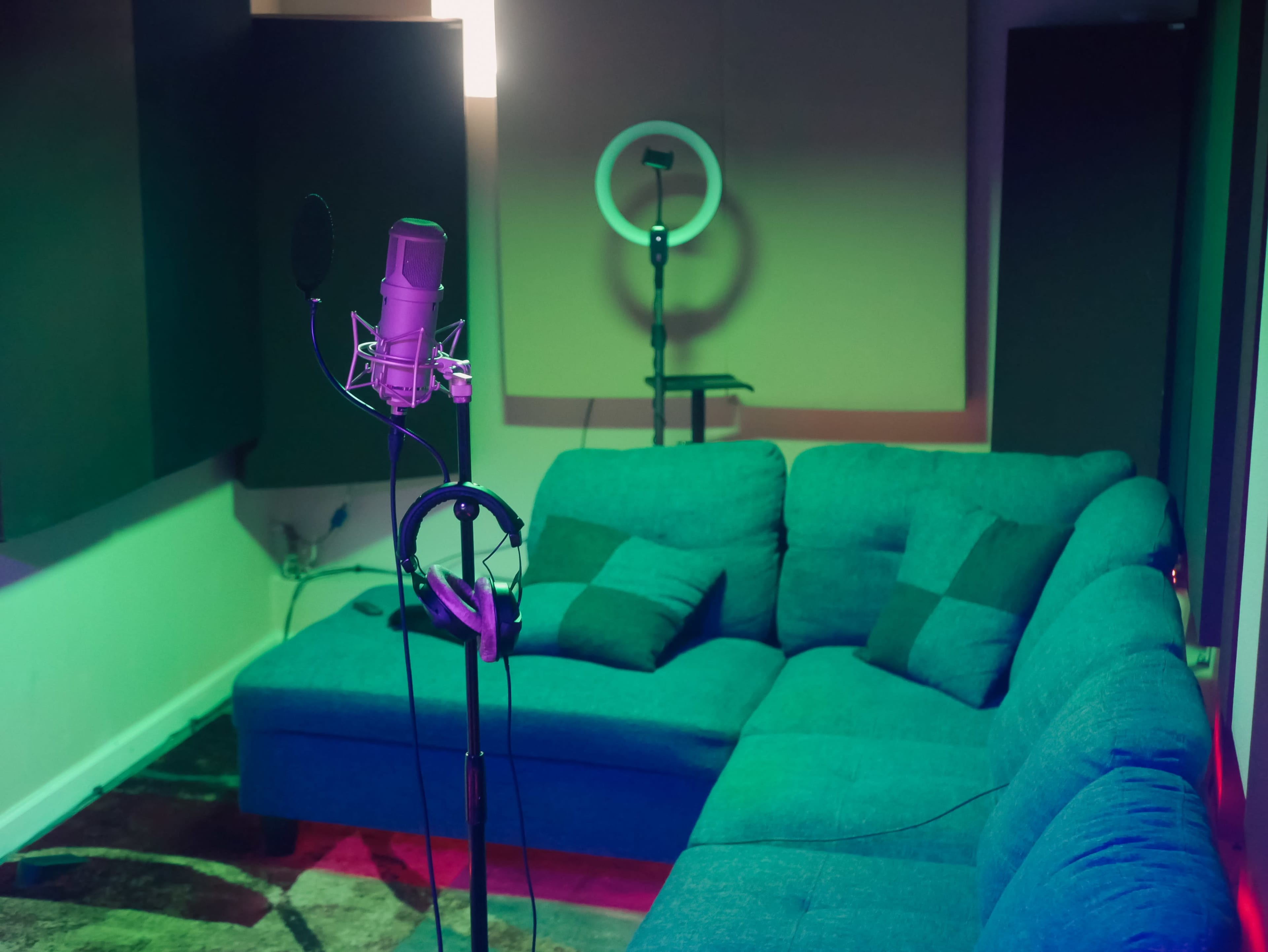 A recording studio with a microphone on a stand, headphones hanging nearby, and a couch in a dimly lit room.