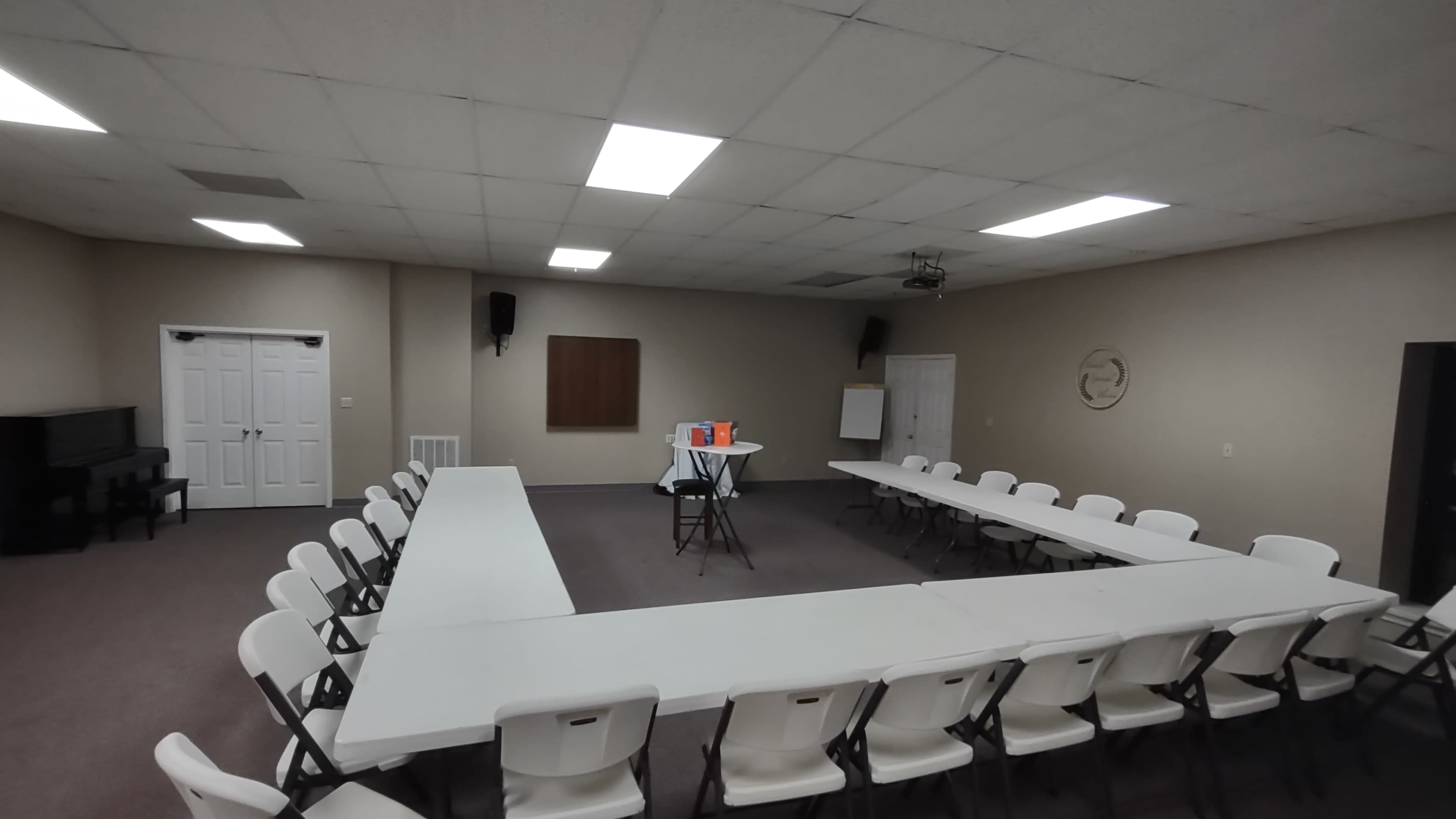 A spacious meeting room features a large rectangular table surrounded by white chairs, with a projector and whiteboard at one end.