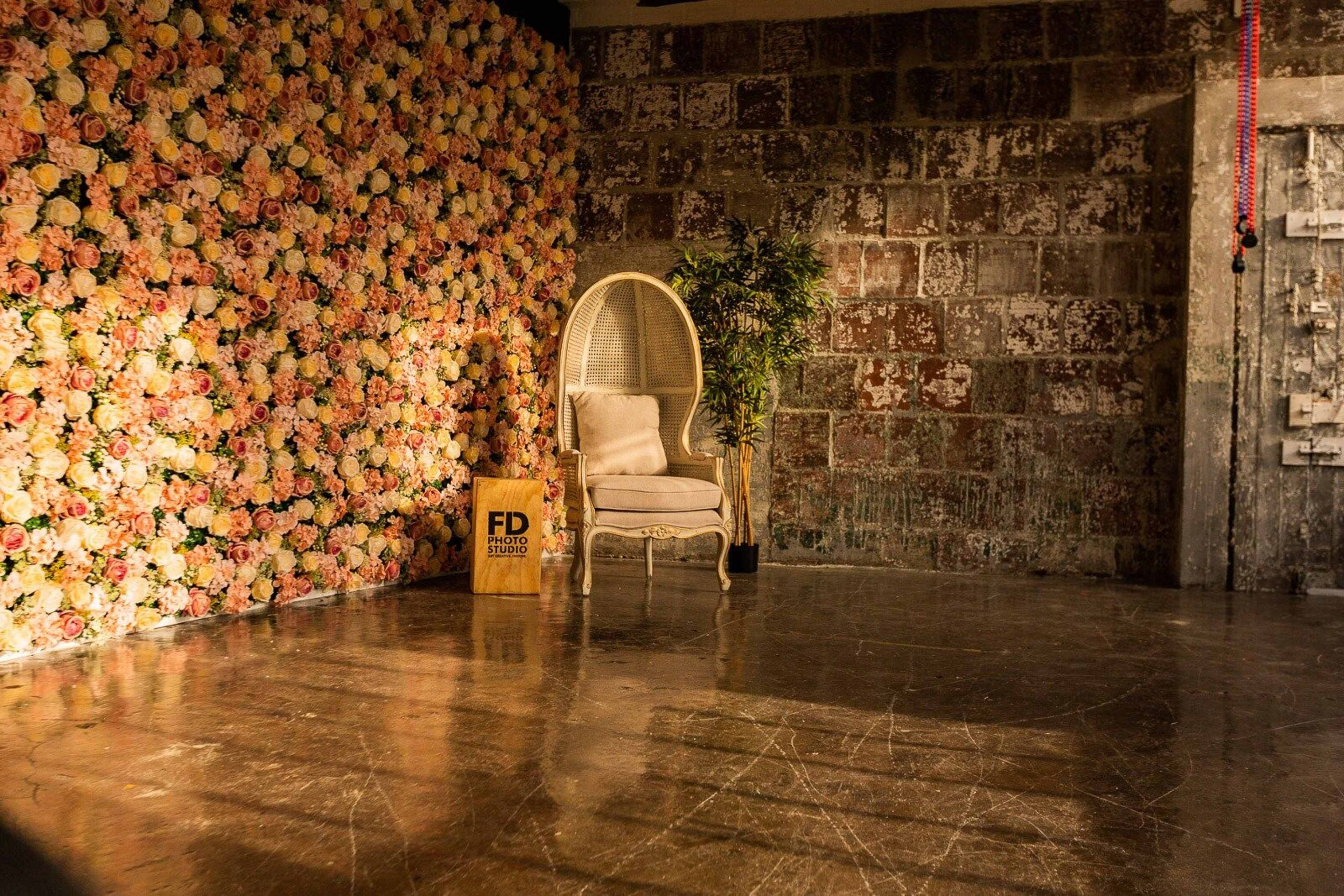 A vintage white chair positioned in front of a wall adorned with a colorful flower arrangement, set in an industrial space with a concrete floor.