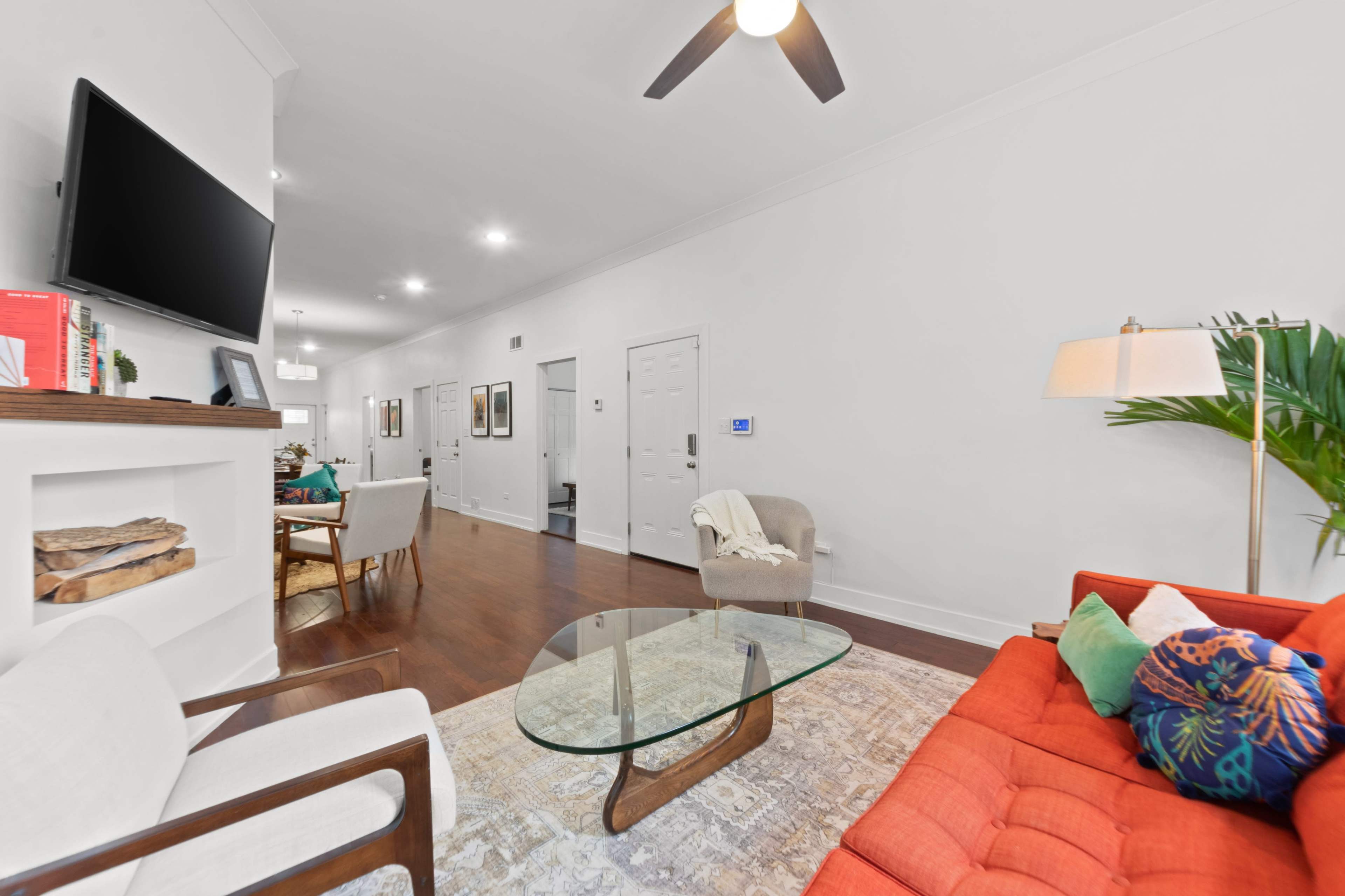 A modern living room features a bright orange sofa, a glass coffee table, and a flat-screen TV mounted on the wall.