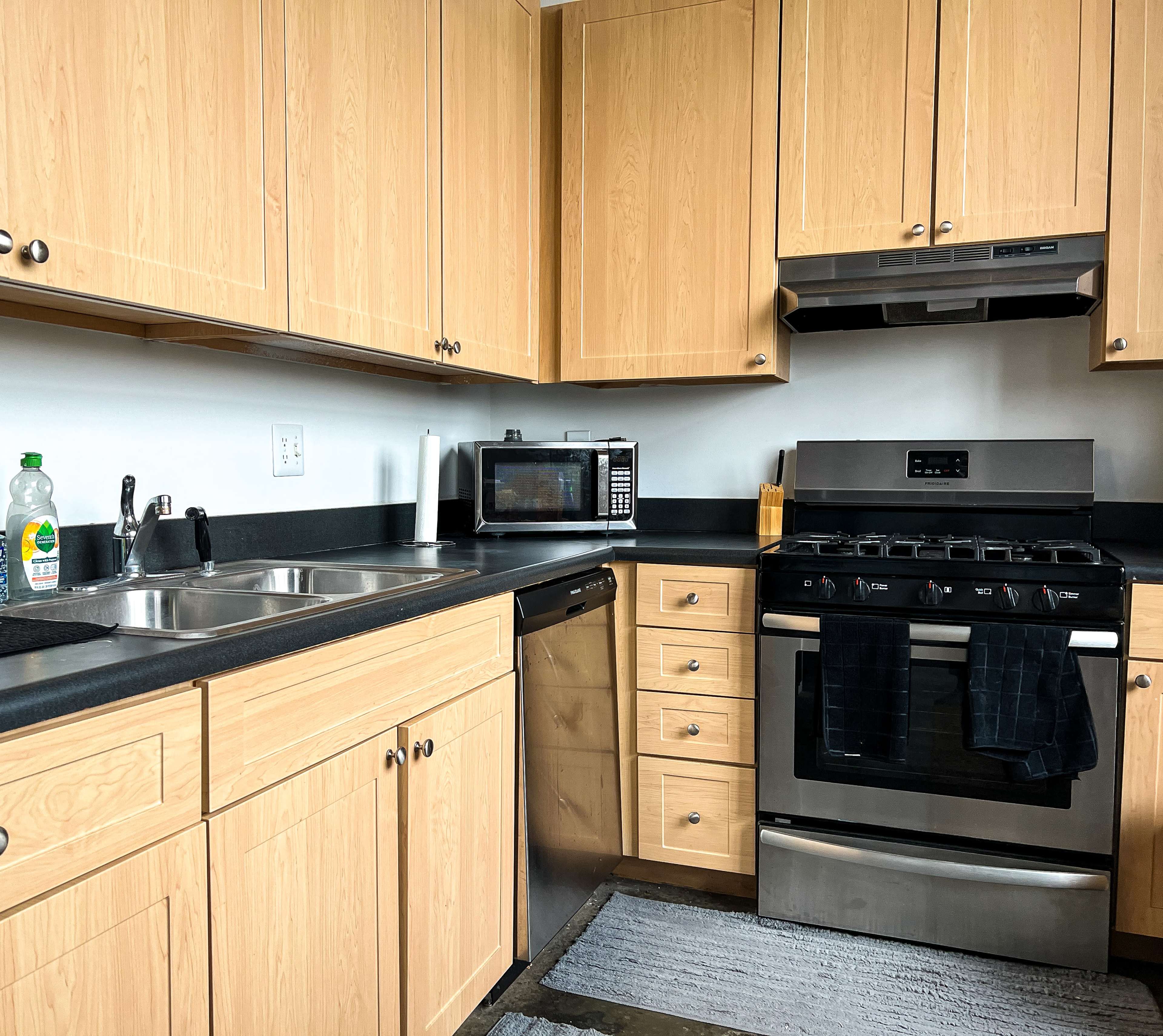 The kitchen features wooden cabinets, a black countertop, a sink, a stainless steel gas stove, a microwave, and a dishwasher.