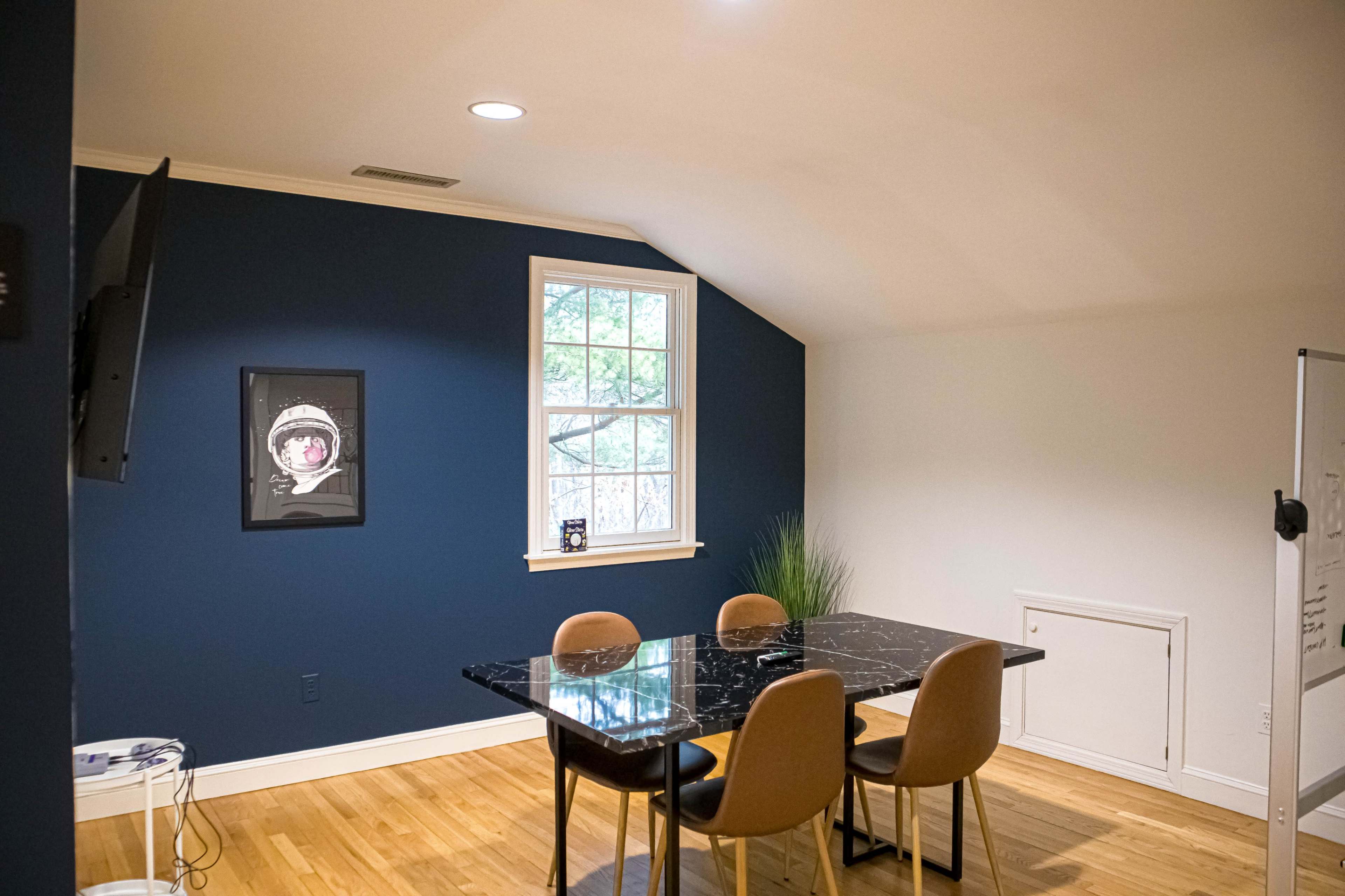 A dining area features a black marble table with four chairs, a large window, and a framed picture on the blue wall.