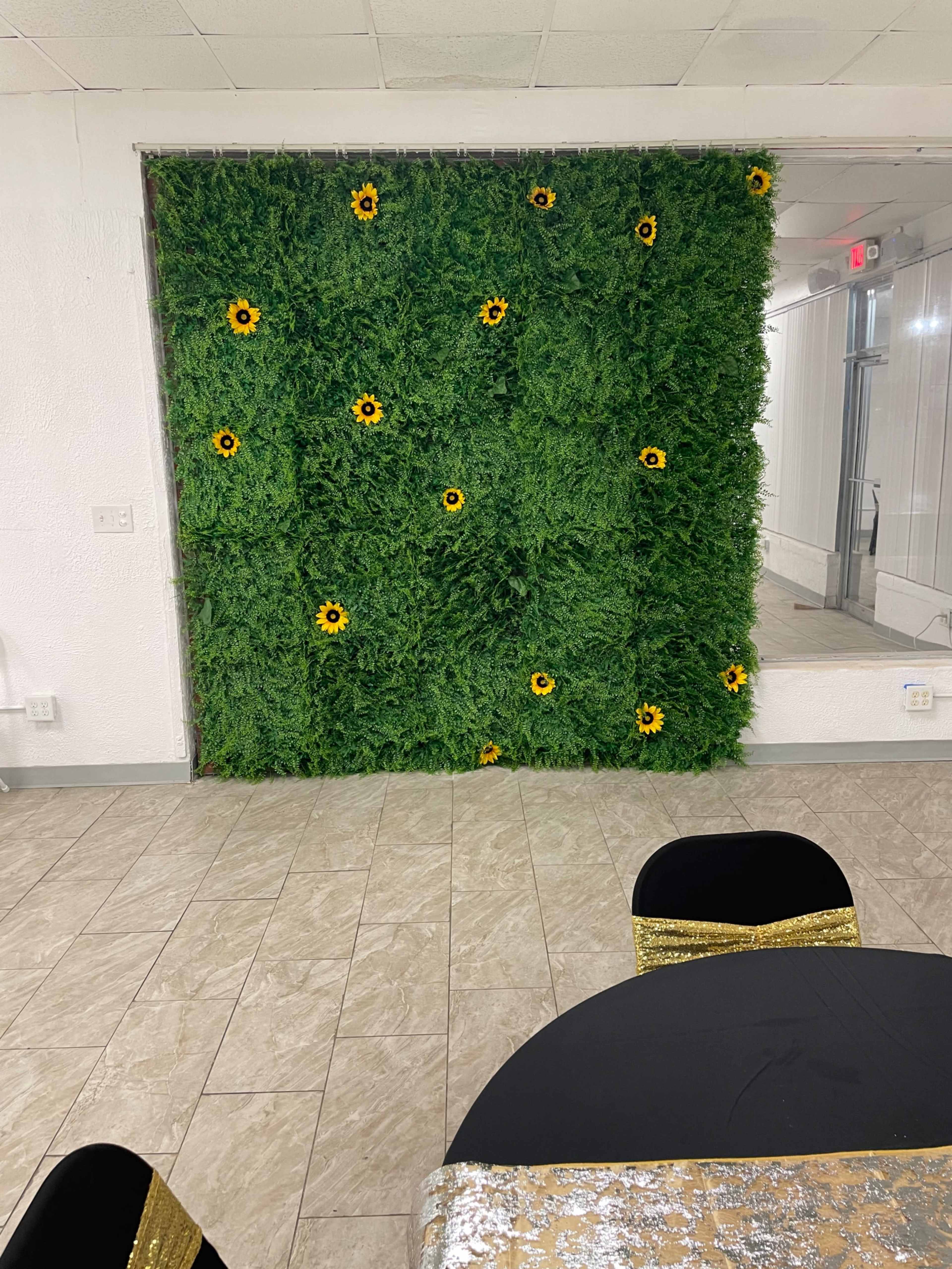 A textured green wall adorned with sunflowers is displayed in a room featuring tiled flooring and a black table covered with a sequin tablecloth.