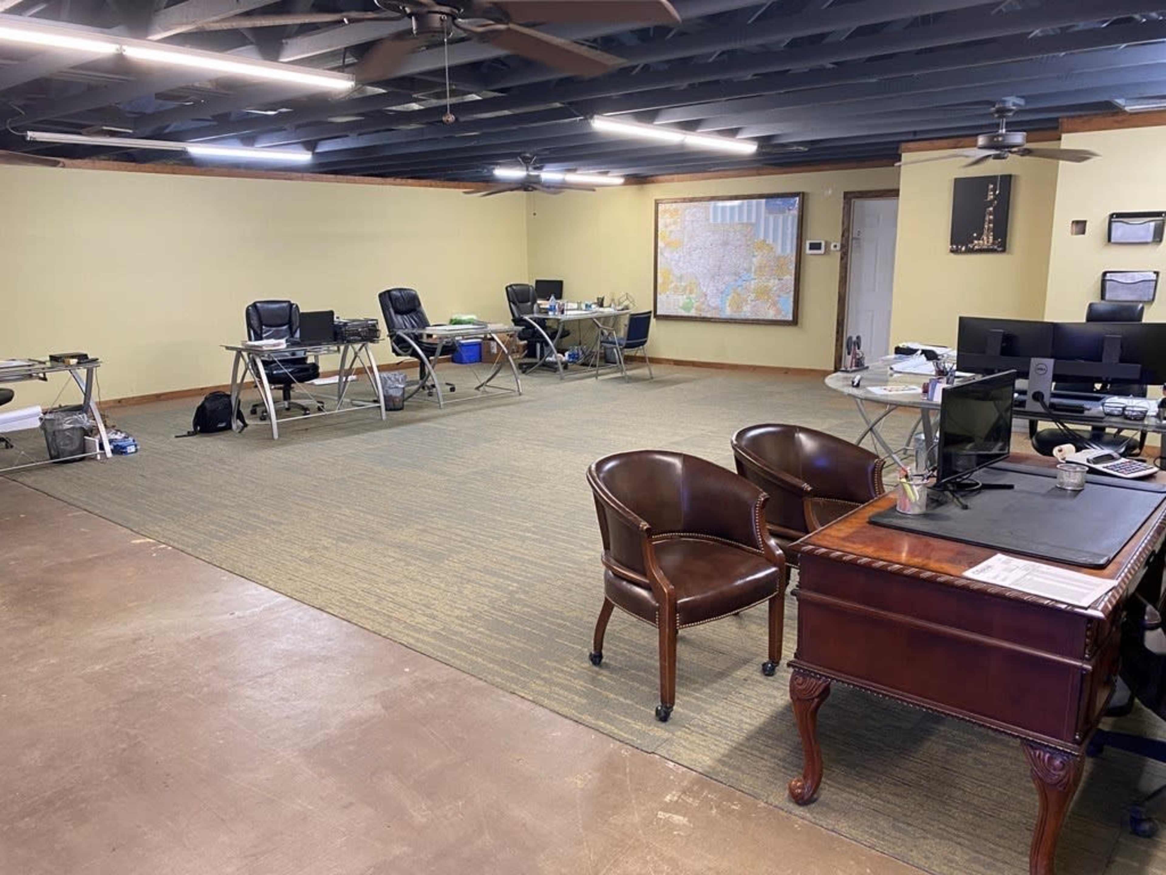The image shows a spacious office space with several desks, chairs, and computers arranged around the room.