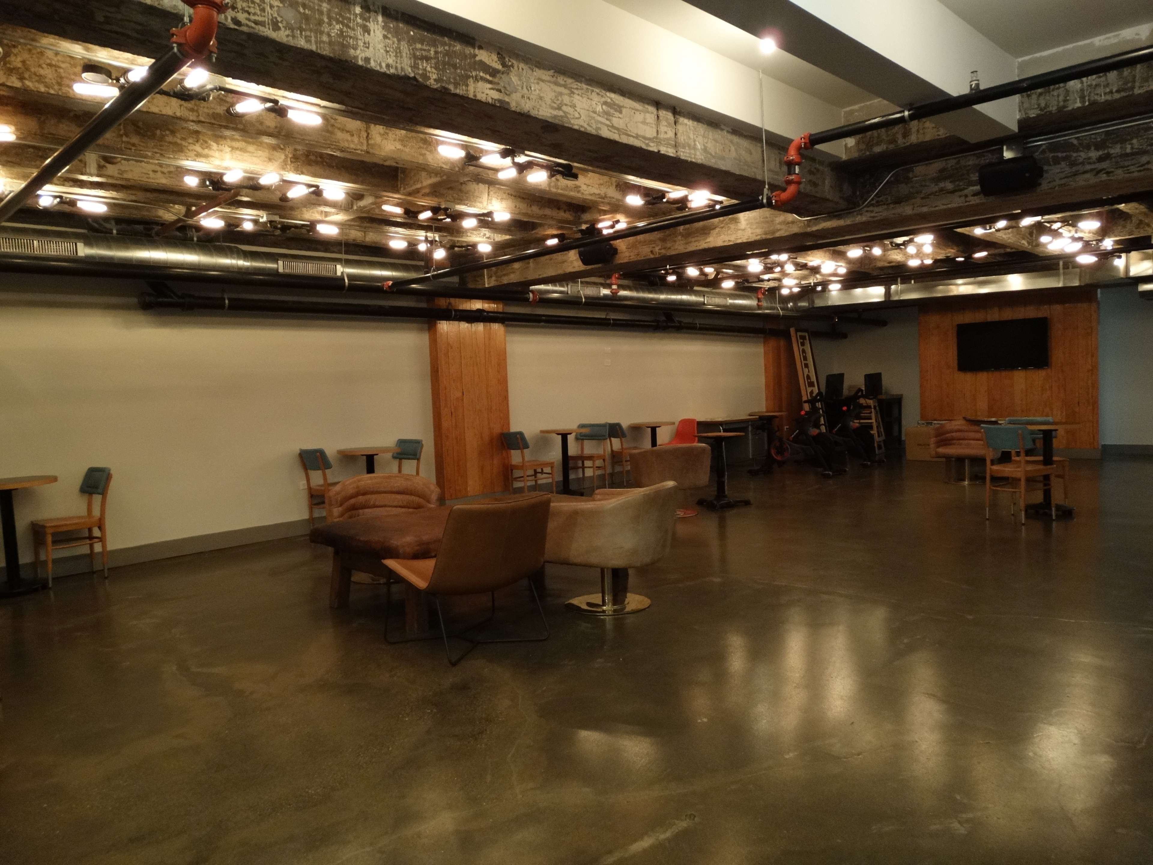 An empty, modern event space with various seating arrangements and exposed lighting fixtures.