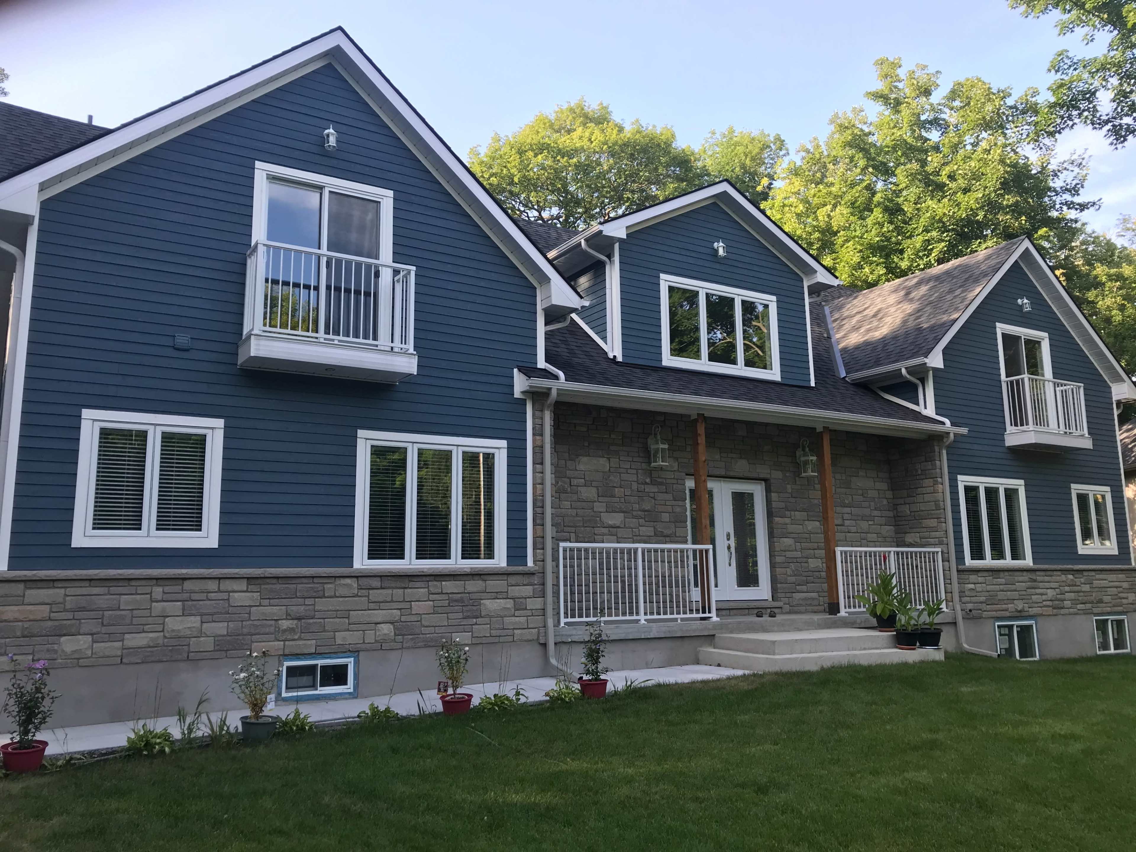 A large, modern two-story house features blue siding and stone accents, with multiple windows and balconies.