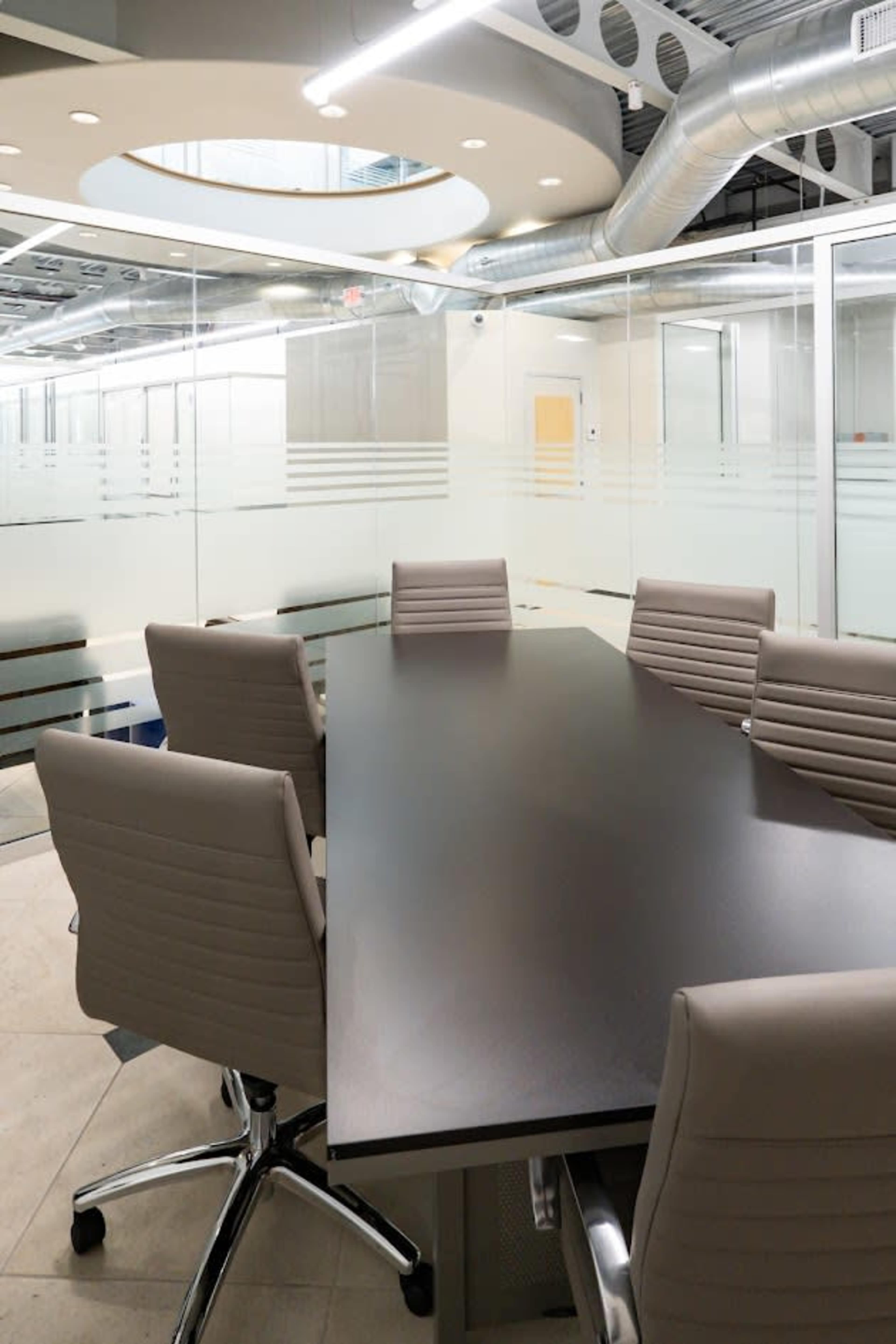 The image shows a modern conference room with a long black table surrounded by light-colored swivel chairs, and glass walls featuring horizontal stripes.