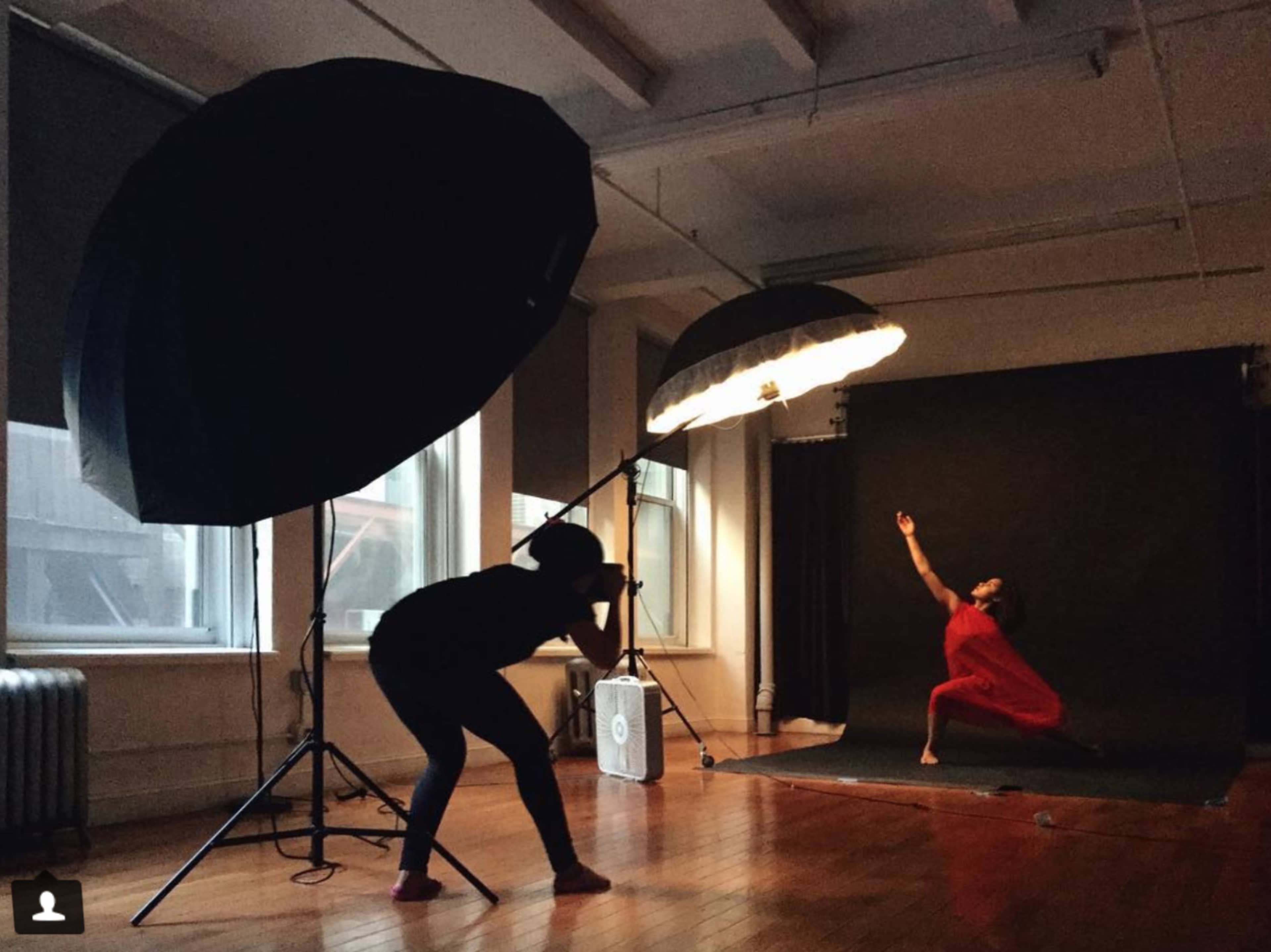 A photographer captures a dancer in a red dress striking a pose in a studio illuminated by large softbox lights.