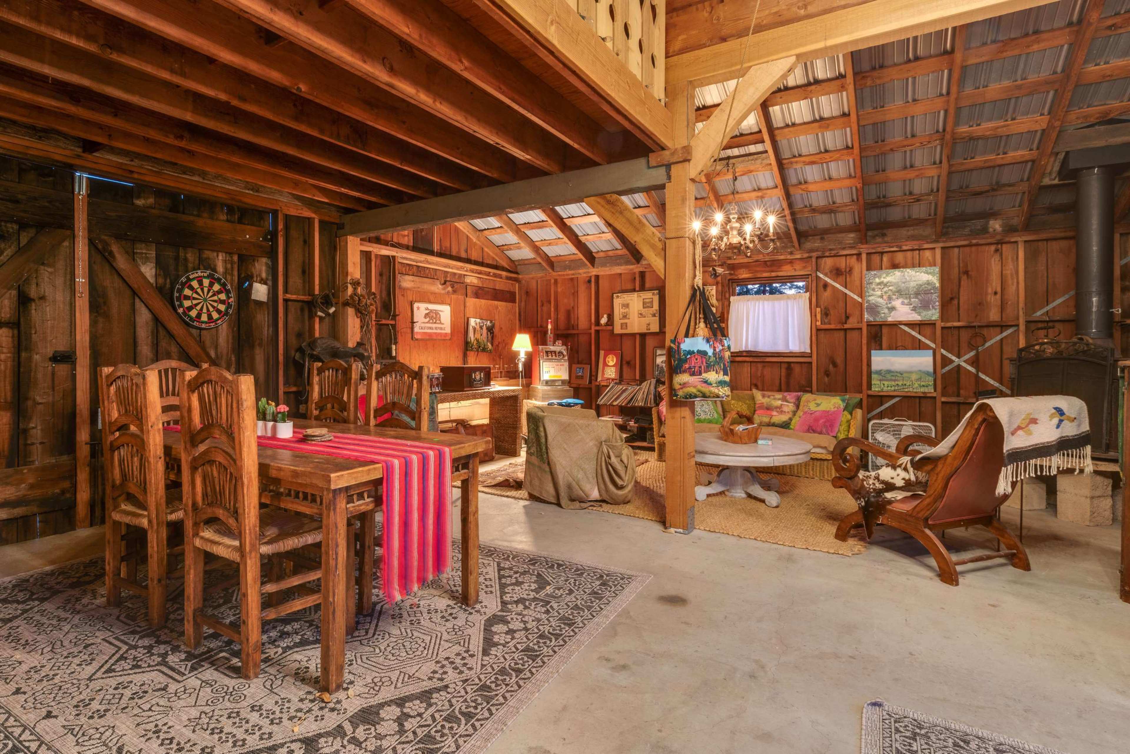 The interior of a rustic cabin features wooden beams, a dining table with chairs, a seating area with a round table, and various decorative elements.