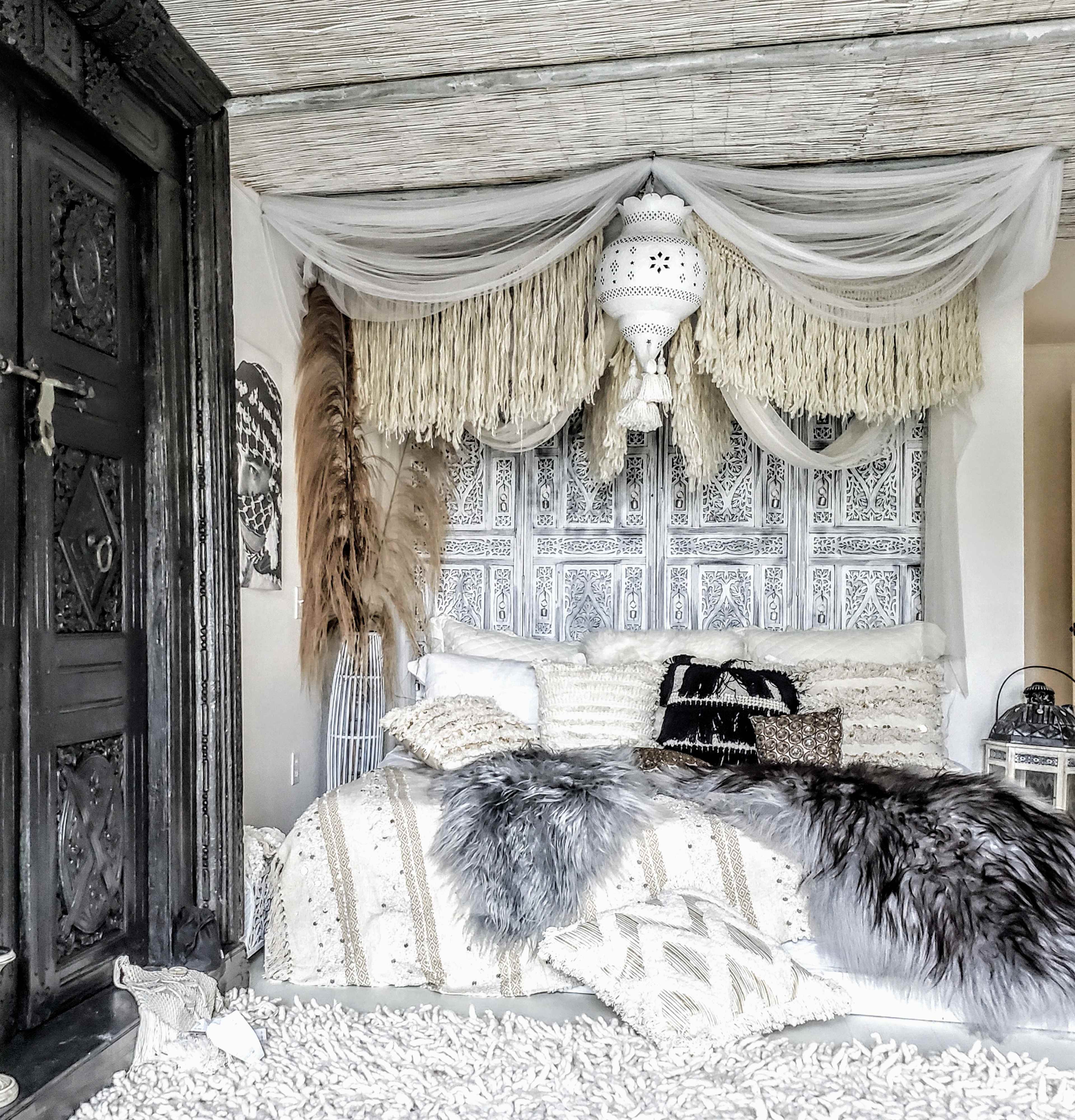 A stylish bedroom with a textured wall adorned with intricate designs, a bed covered in various decorative pillows and throws, and a lantern hanging above.
