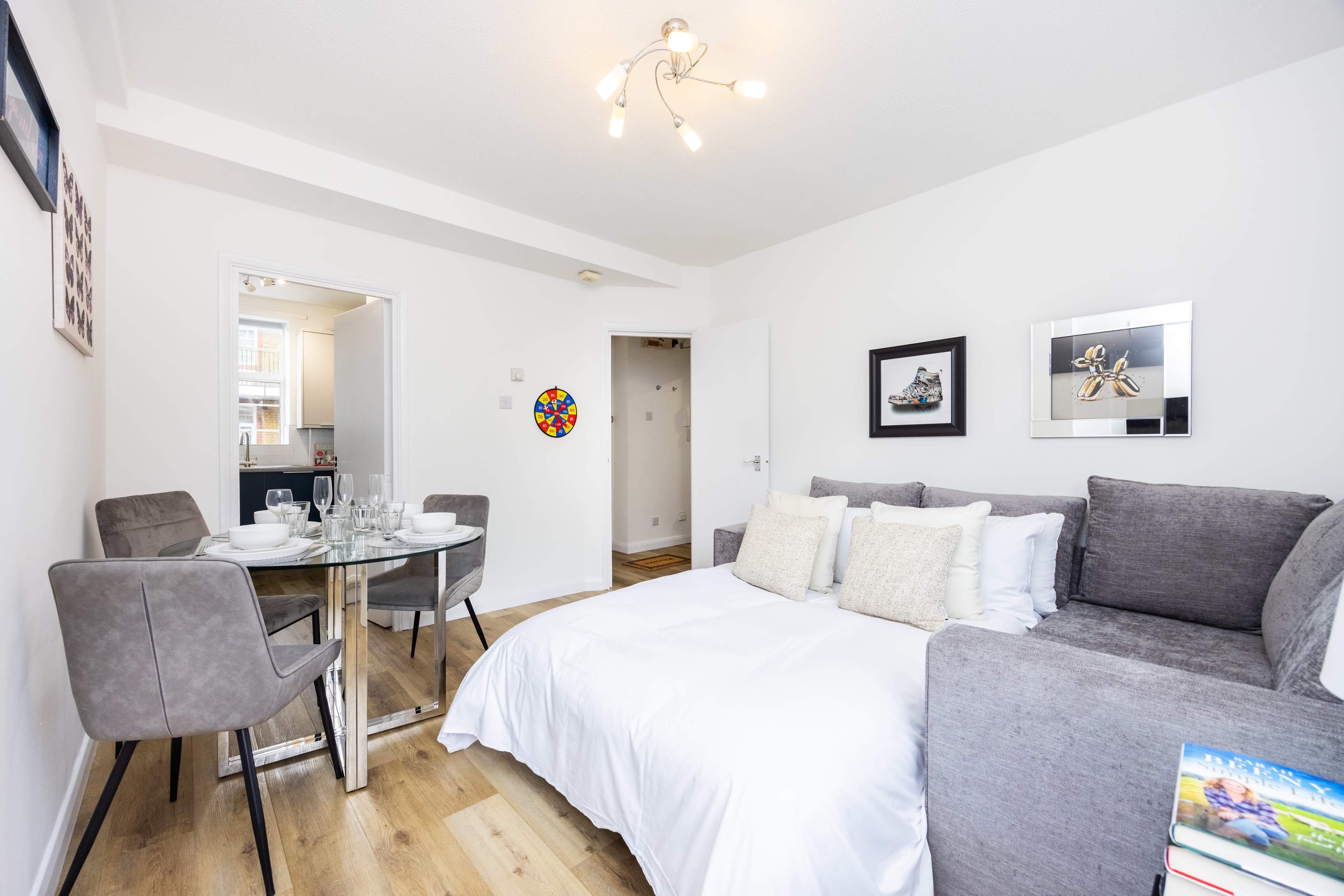 The image shows a modern living space with a gray sofa bed and a round dining table set for four.