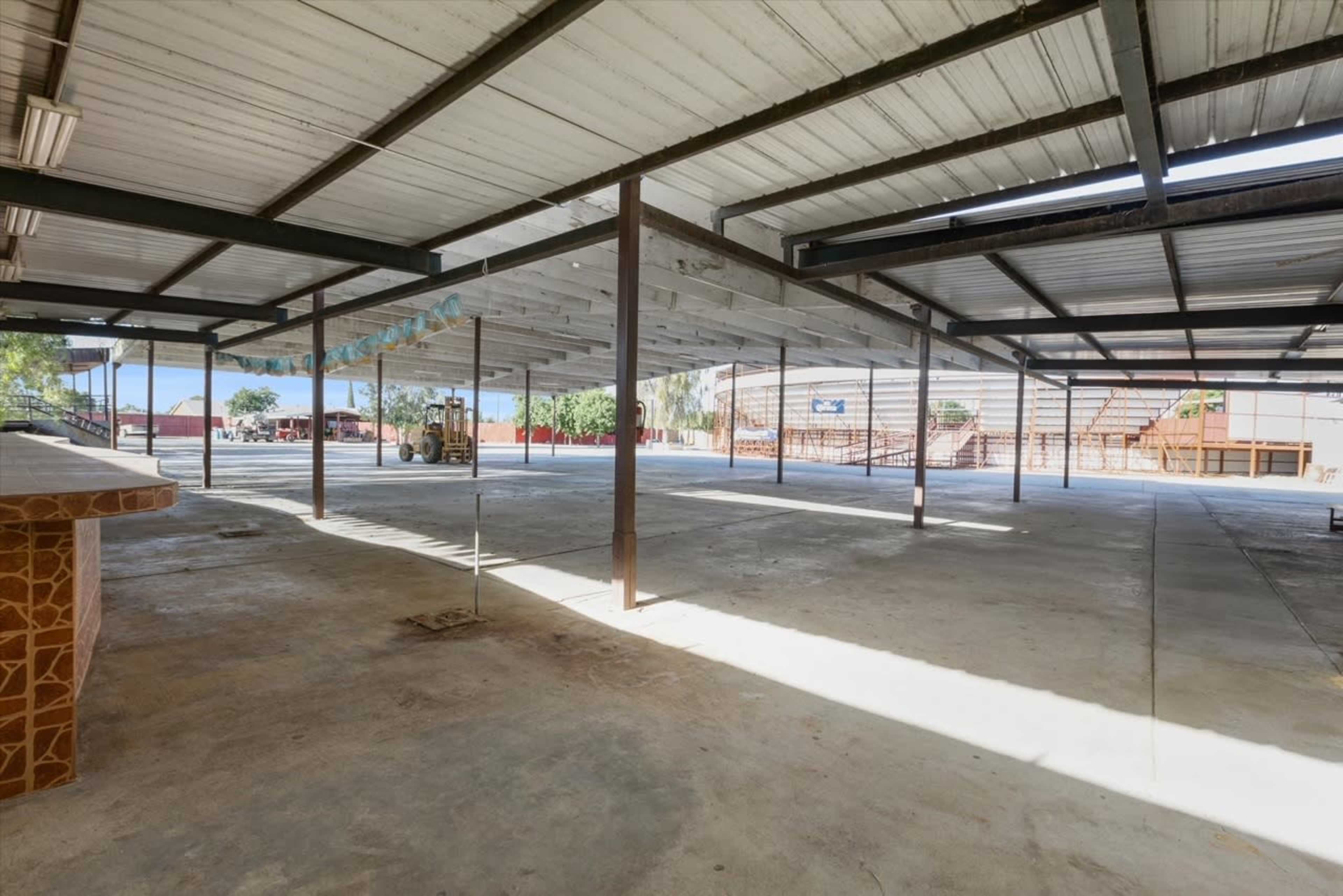 A large, open, industrial-style space with a concrete floor and metal beams supporting a roof.