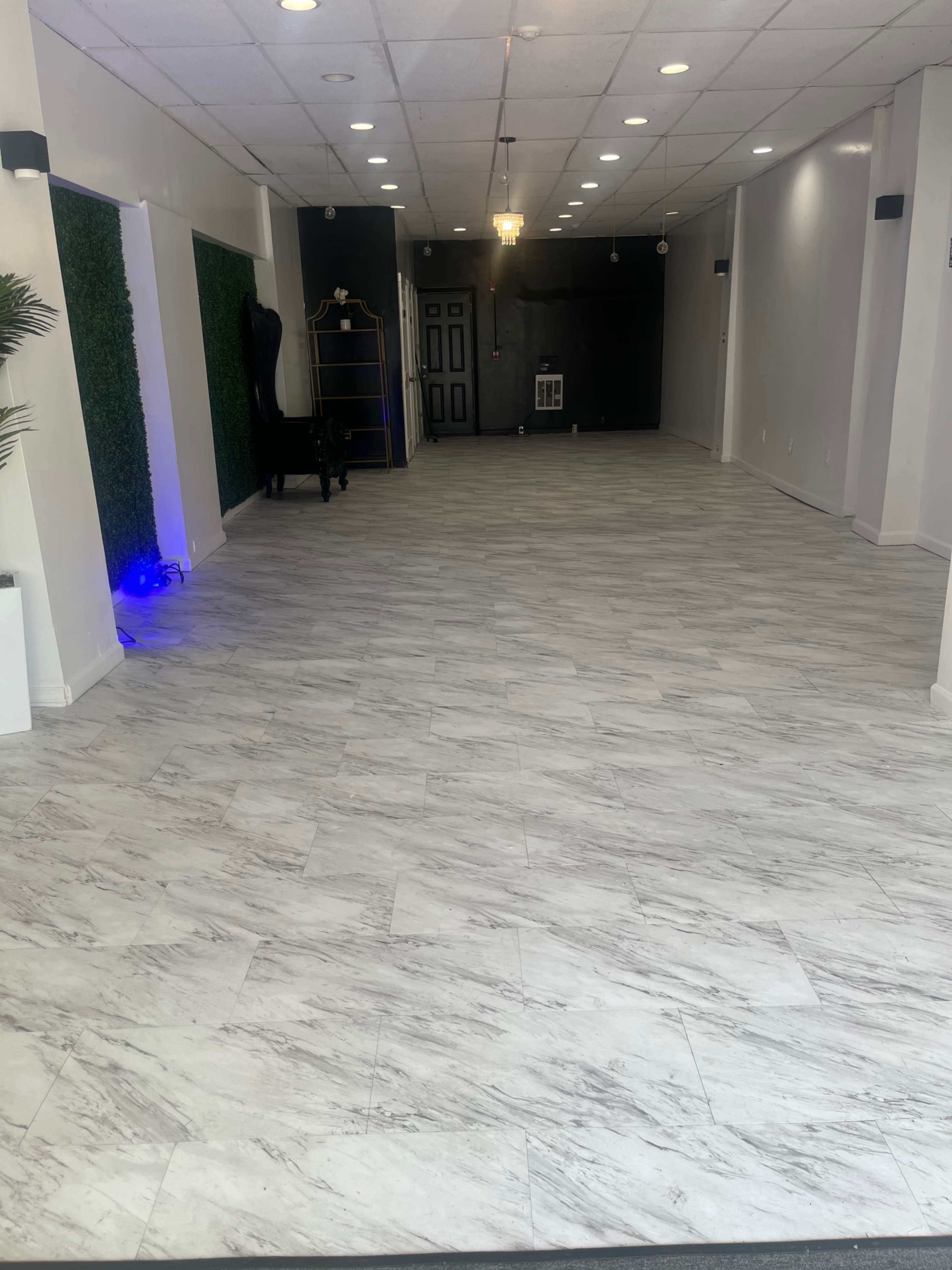 A spacious interior room with marble-patterned flooring and minimalist decor, featuring a black wall at the far end.