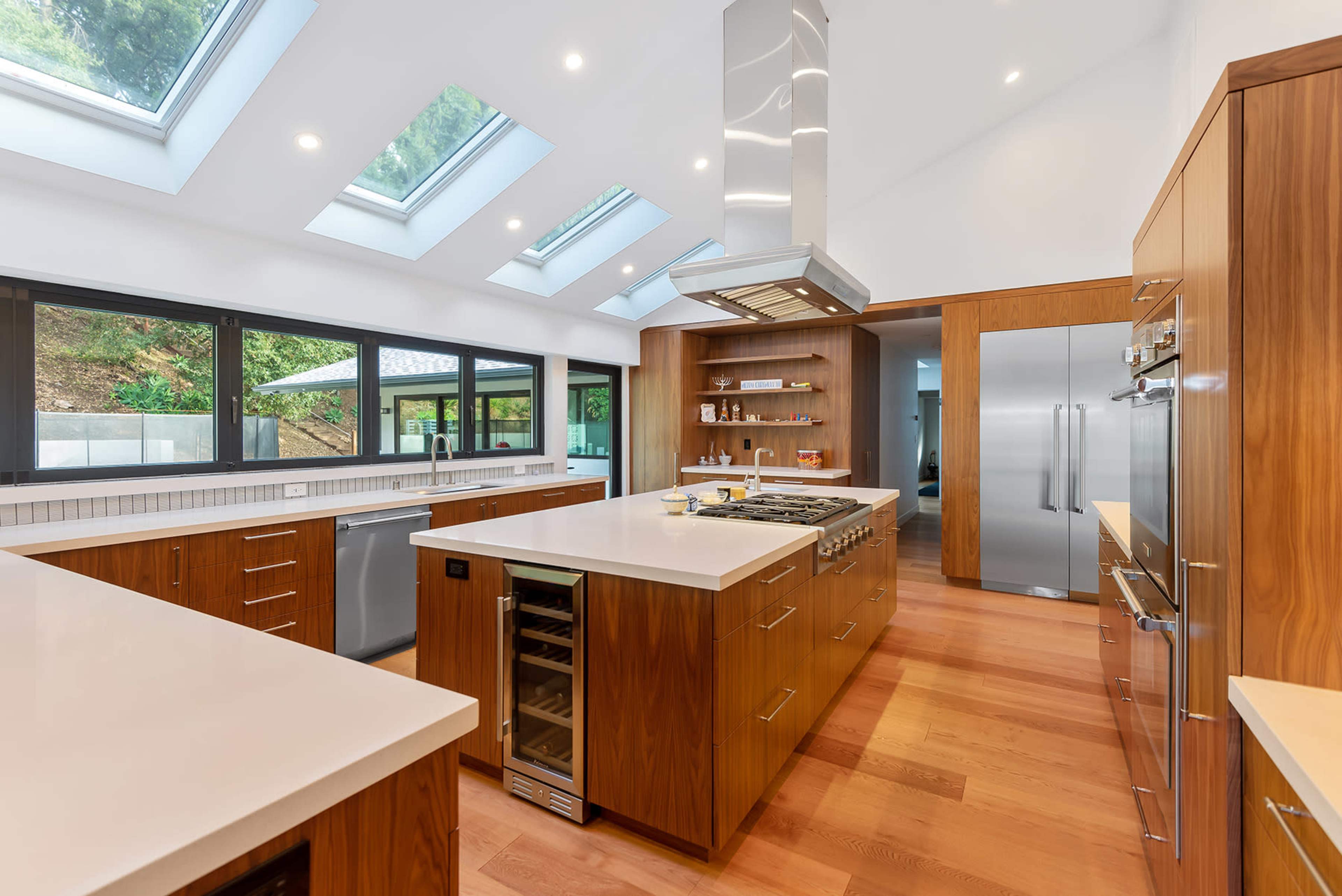 A modern kitchen features a central island with a stovetop, equipped with wooden cabinetry and large skylights above.
